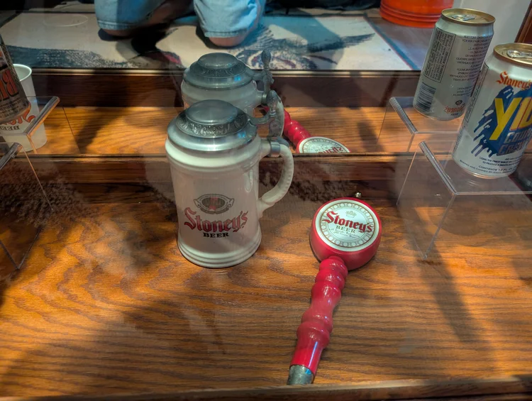 Vintage Stoney's Beer ceramic stein and red tap handle on a wooden display shelf