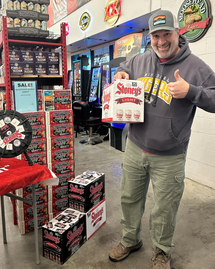 A customer giving a thumbs-up at a Stoney's Beer tasting at Hampton Beer Outlet in Allison Park, Pennsylvania, holding a six-pack of Stoney's Light