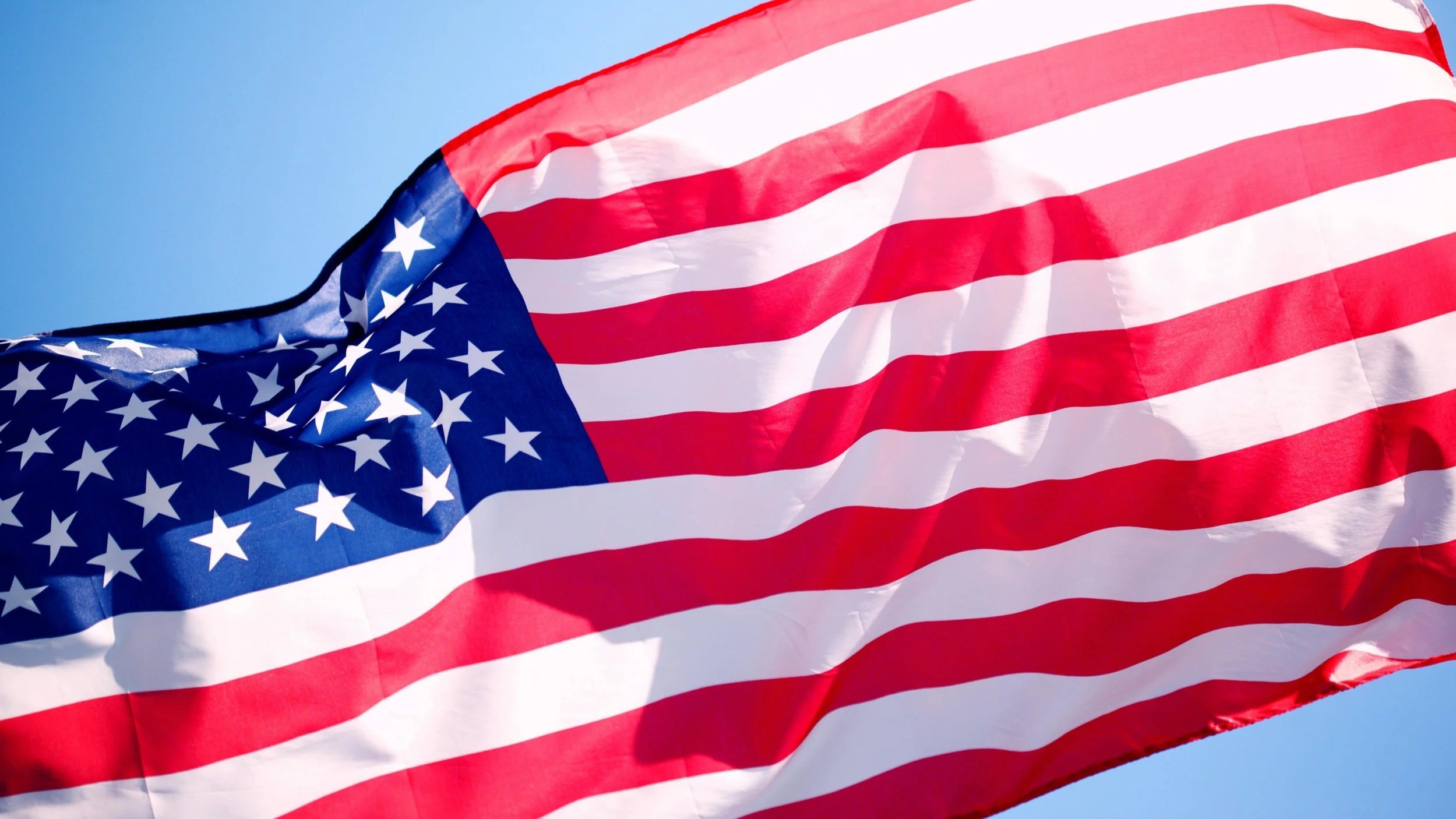 An American flag waving in the wind against a clear blue sky.