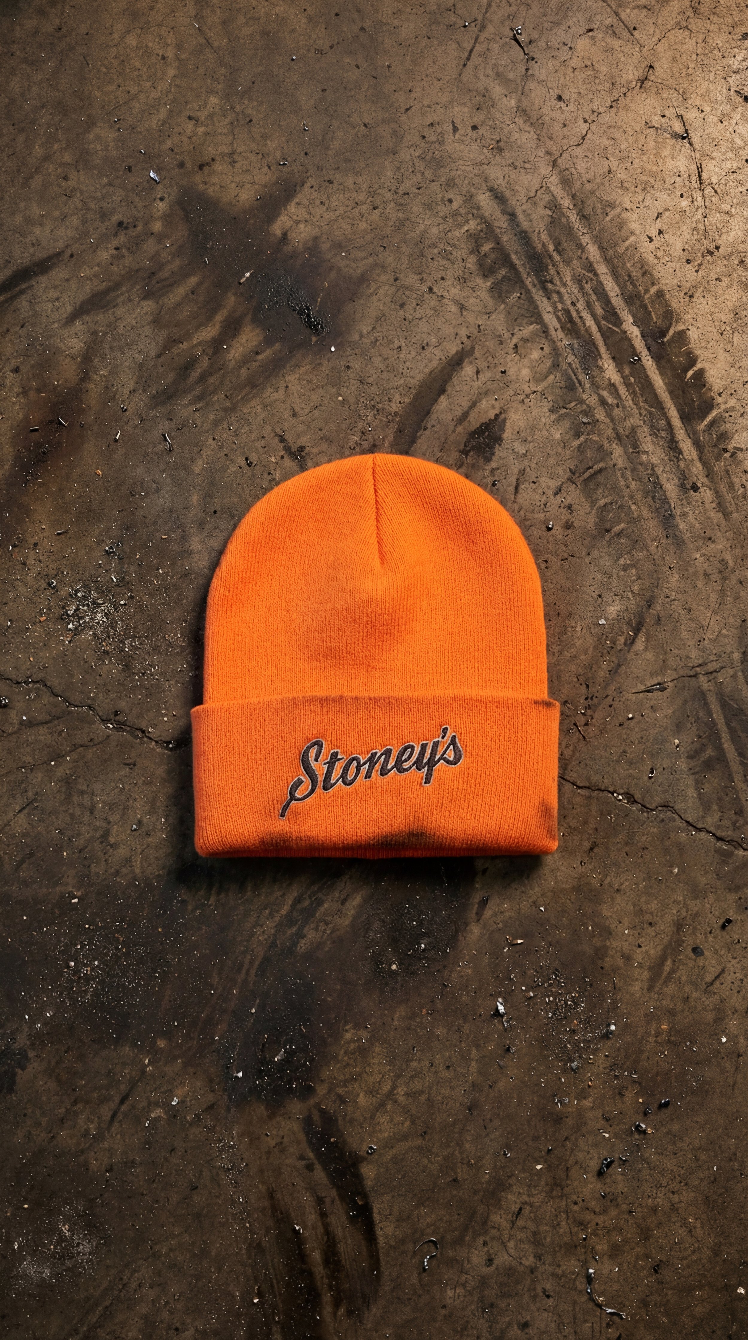 Stoney’s Built To Work orange knit beanie with embroidered logo on rugged jobsite surface in Pennsylvania