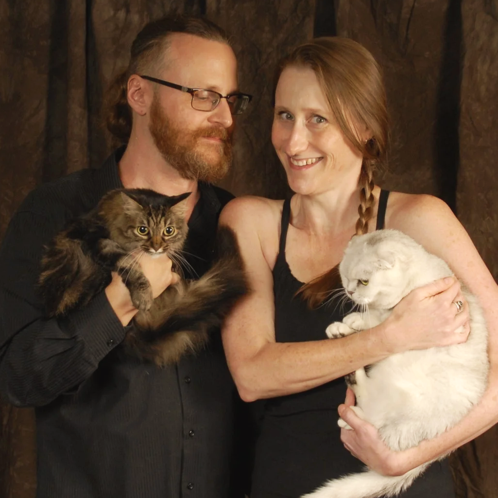 Independent authors Michael R. Swanson & Amanda K. King posing for author photos while holding cats, long haired tabby Squidget and white Scottish Fold Boodle.