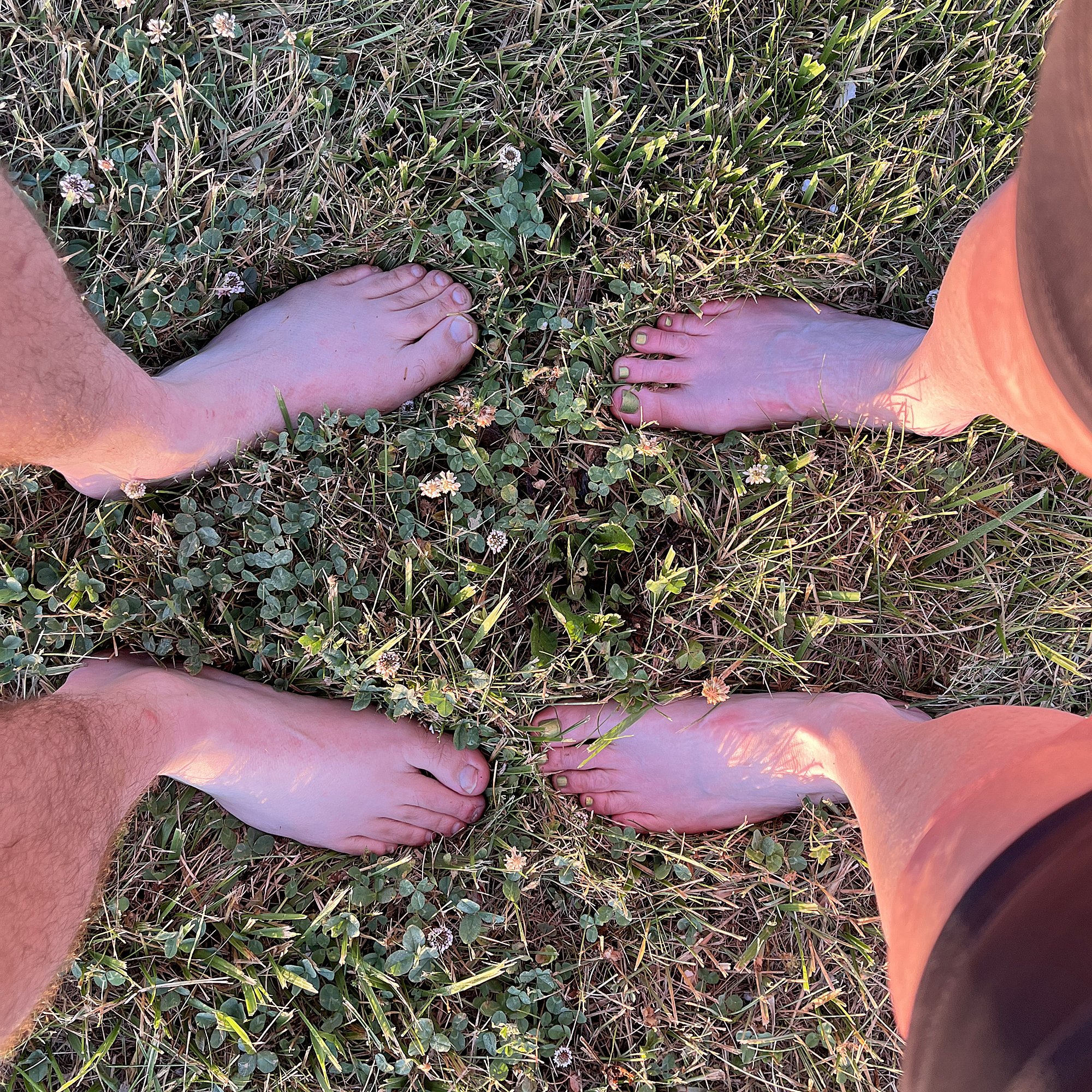 The legs and feet of independent authors Amanda K. King & Michael R. Swanson, standing in grass.