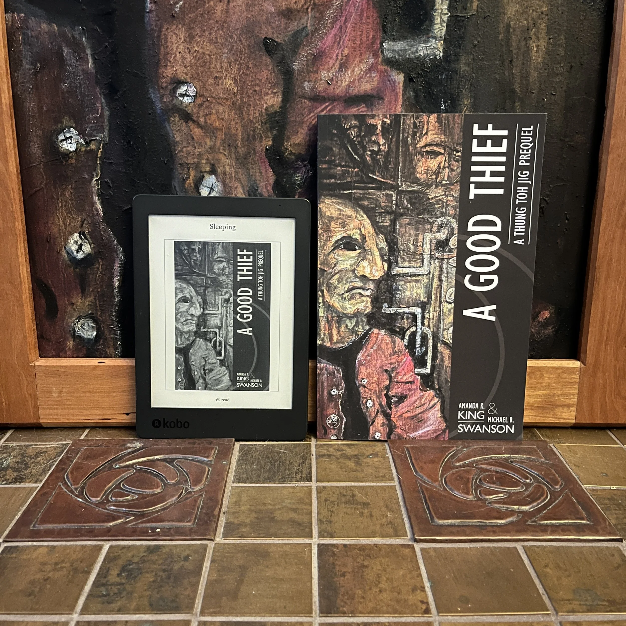 A Good Thief novella by Amanda K .King and Michael R. Swanson sitting in front of the cover painting by Michael B. Fee