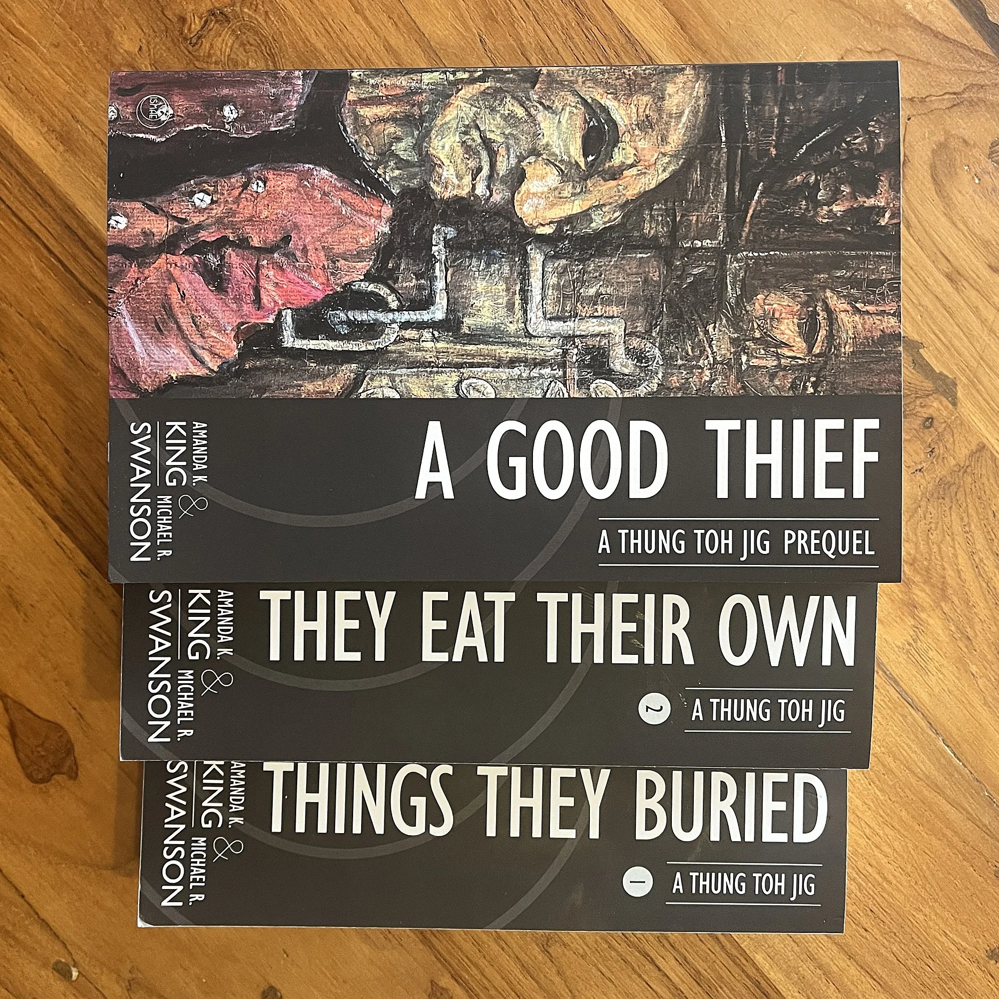 A Good Thief novella trade paperback stacked with series novels Things They Buried and They Eat Their Own