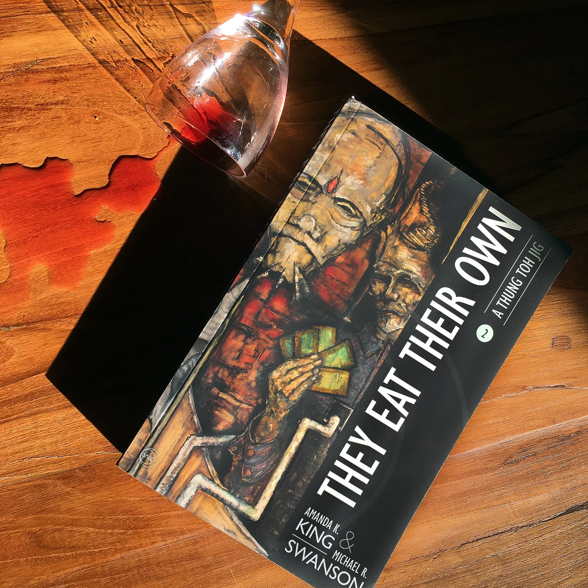 They Eat Their Own trade paperback with a spilled glass of red wine