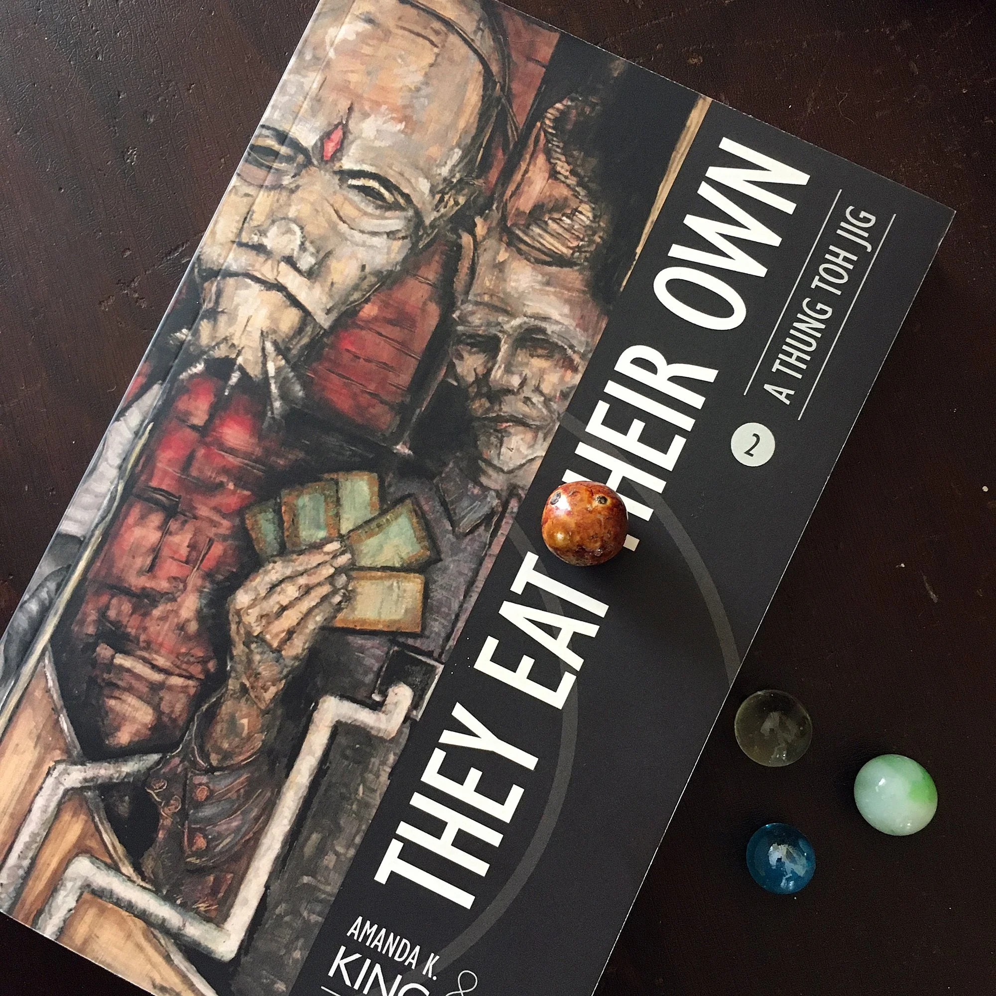 They Eat Their Own trade paperback with a set of gaming marbles