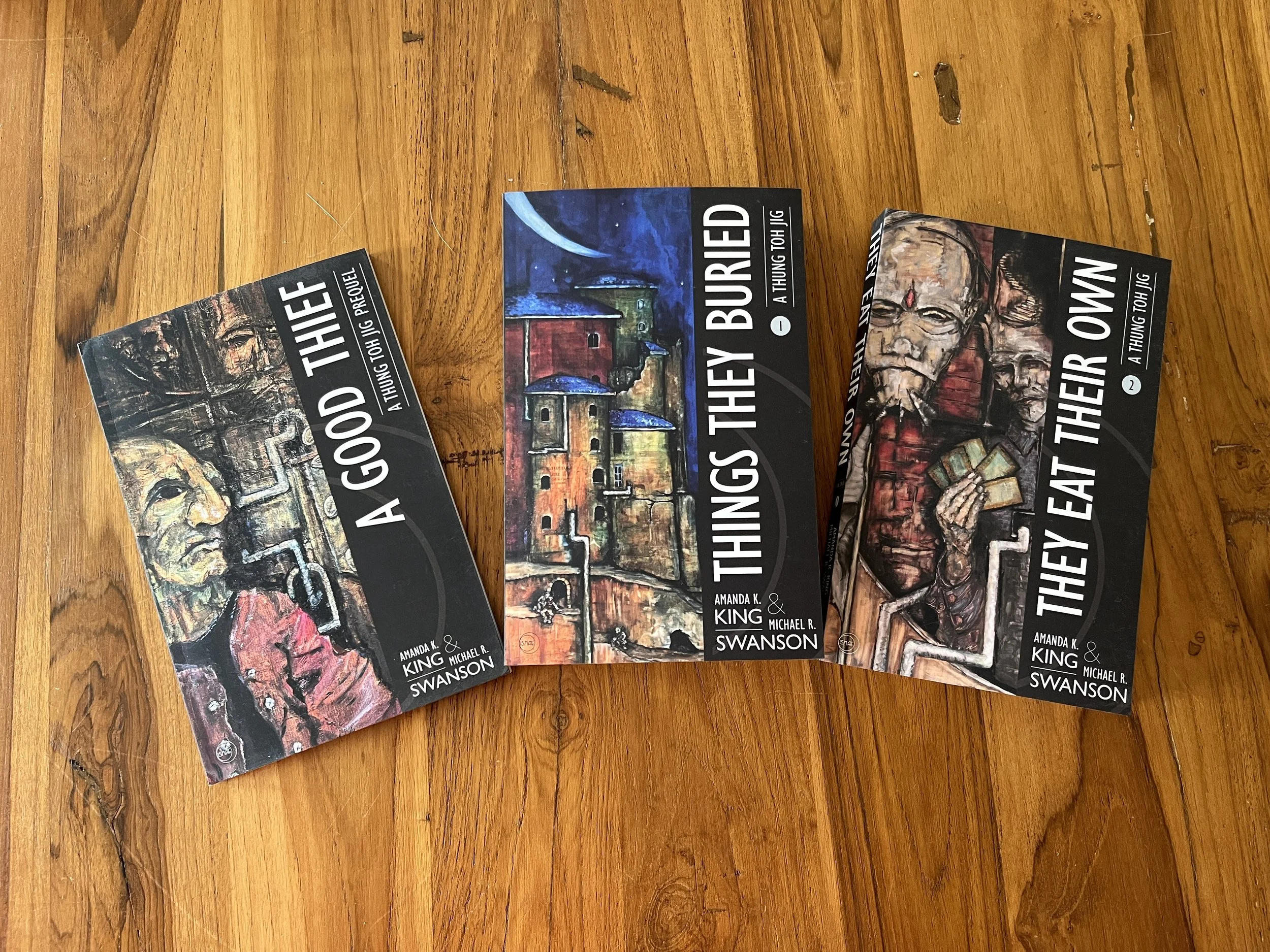 A Good Thief novella trade paperback arrayed with series novels Things They Buried and They Eat Their Own