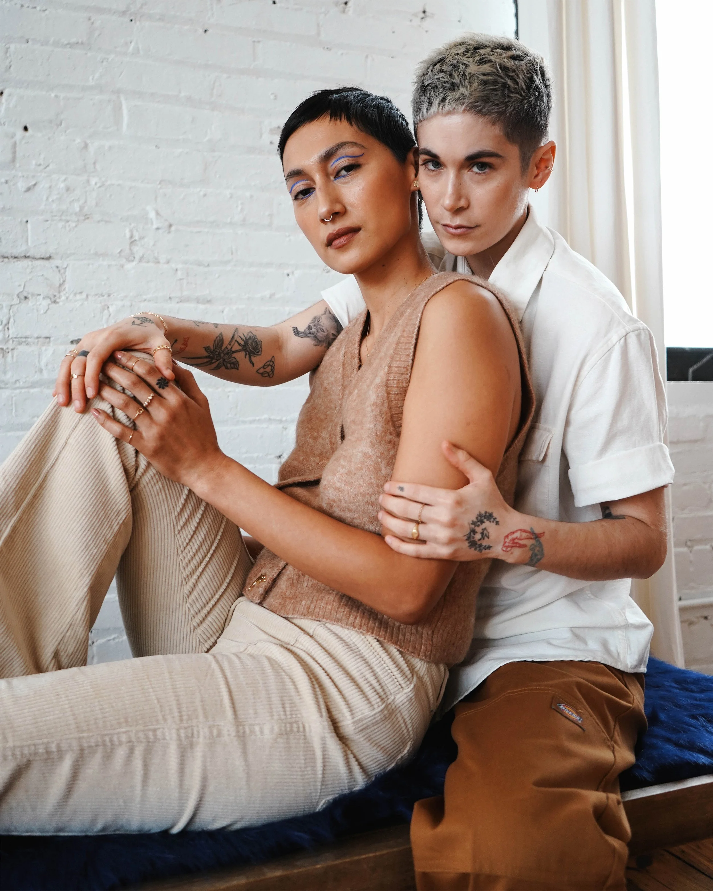 Editorial studio photograph of an LGBTQ+ couple styled with jewellery, highlighting intimacy and modern fashion aesthetics.