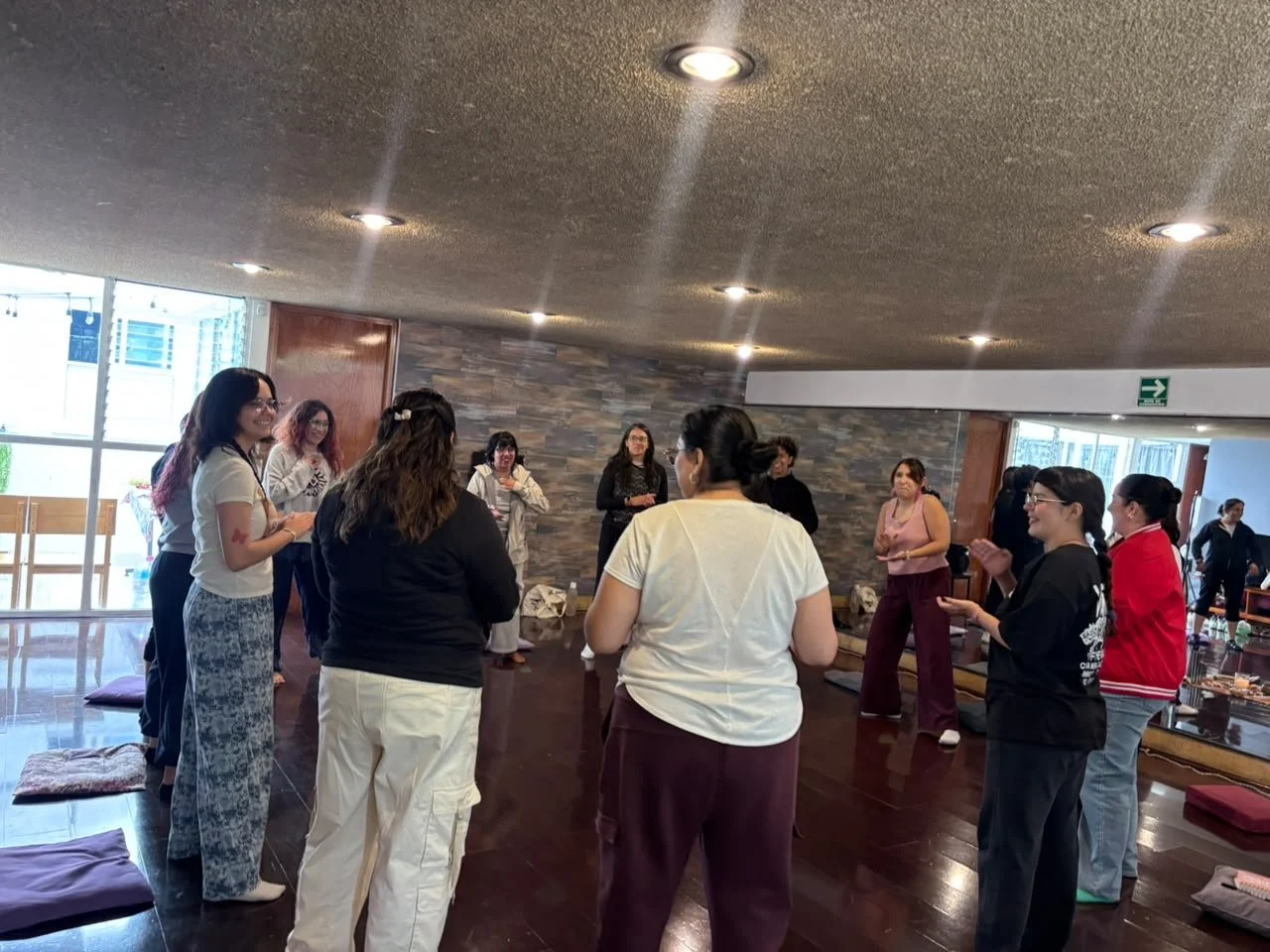 Grupo de personas en una sala, algunas con ropa casual, participando en una actividad de estilo  arteterapia  o meditación, con colchonetas en el suelo