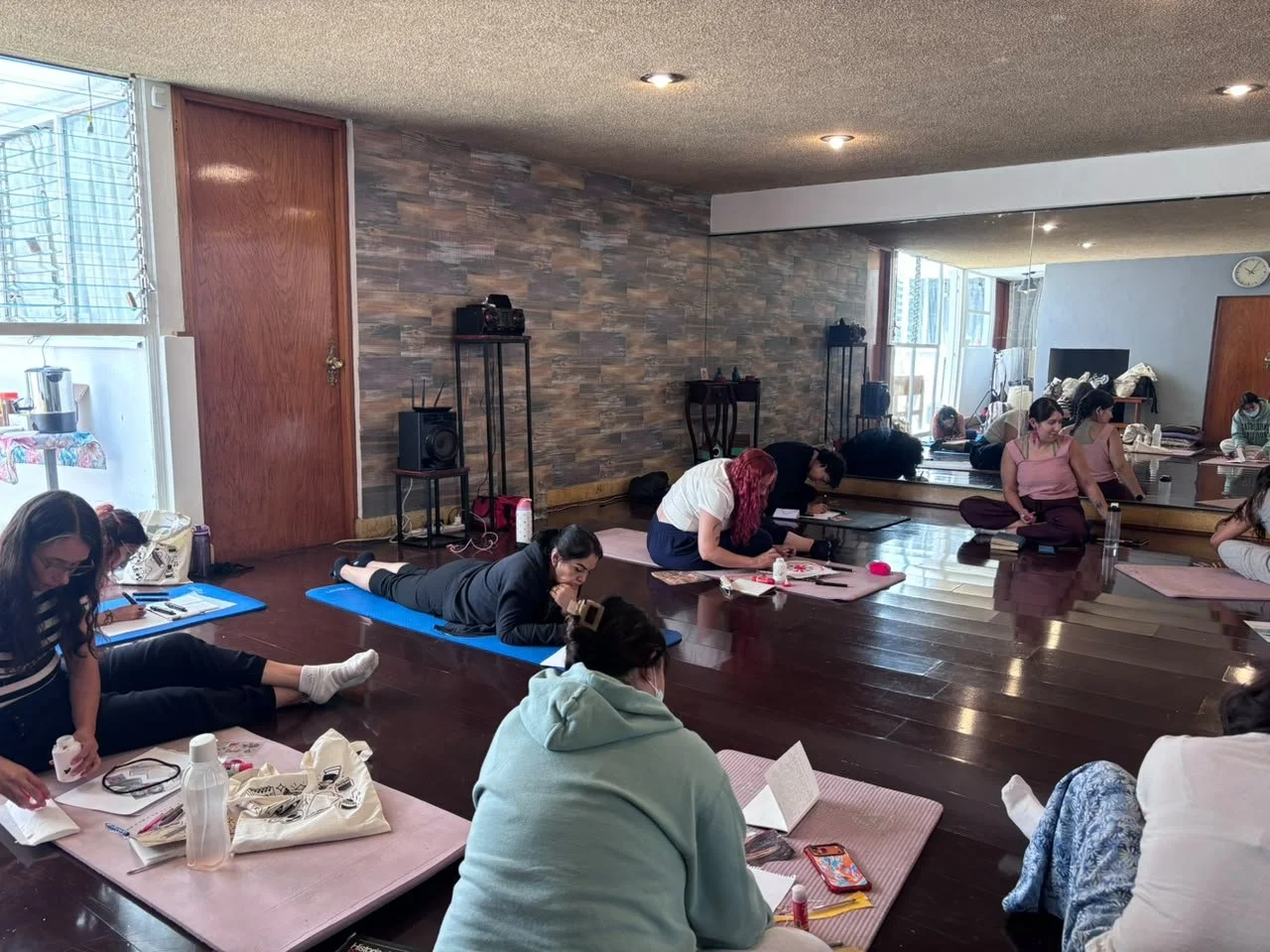 Grupo de mujeres participando en clase de arteterapia en una sala con espejo y piso de madera.