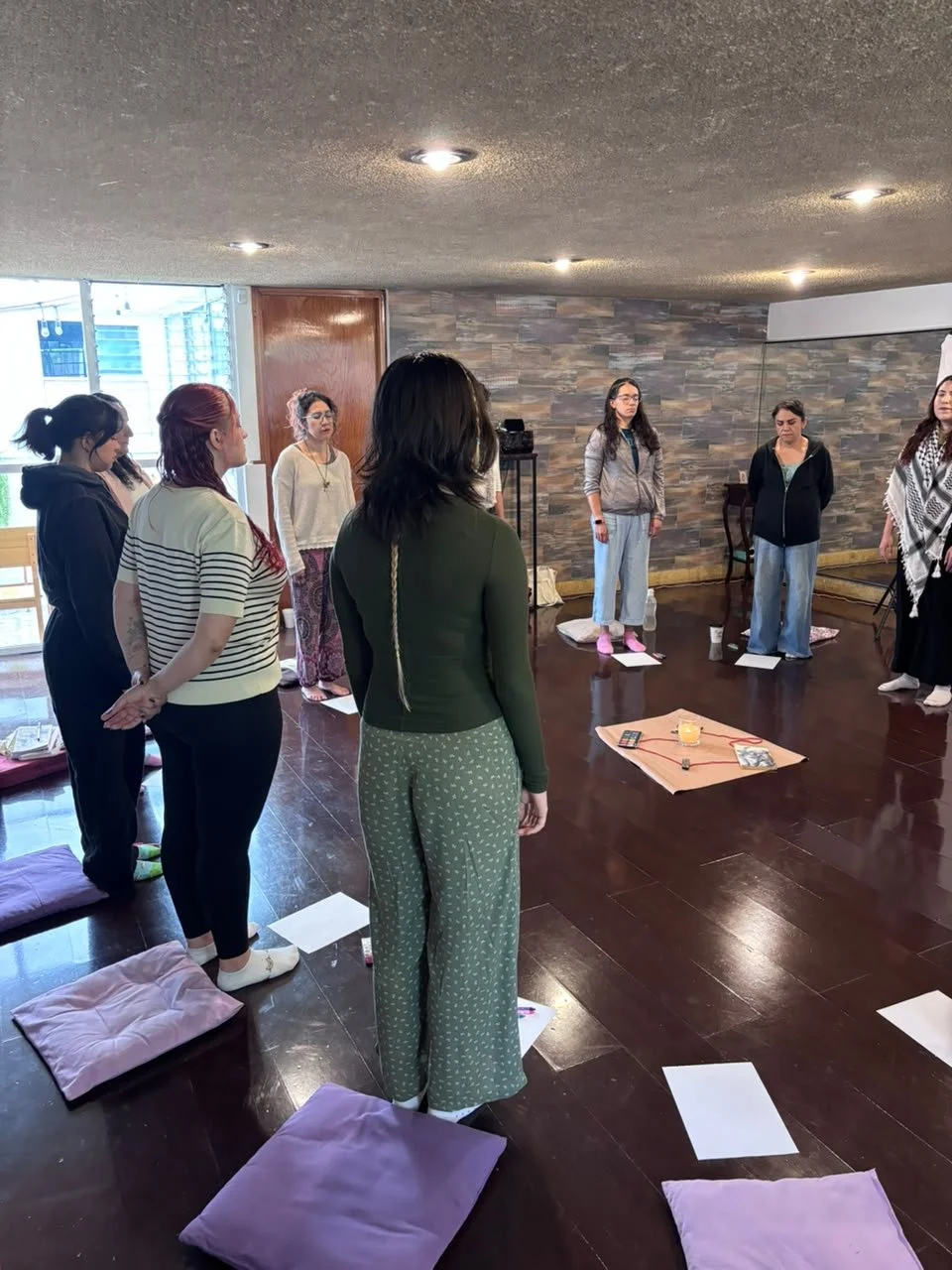 Grupo de mujeres en una reunión espiritual o de meditación, con colchonetas y almohadas en un ambiente interior.