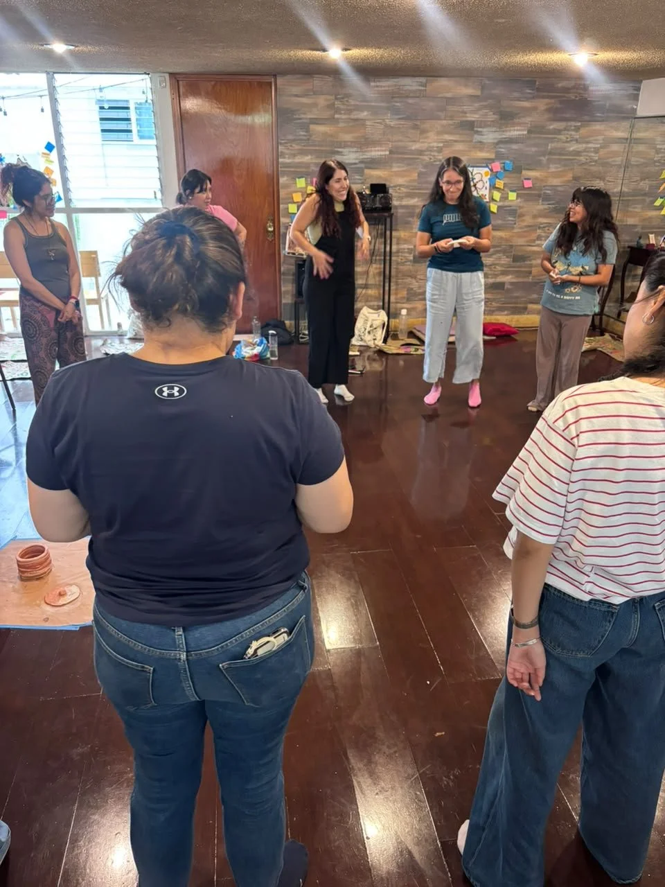 Grupo de mujeres participando en una actividad o taller en un espacio interior con paredes de piedra y muchas notas adhesivas en la pared.