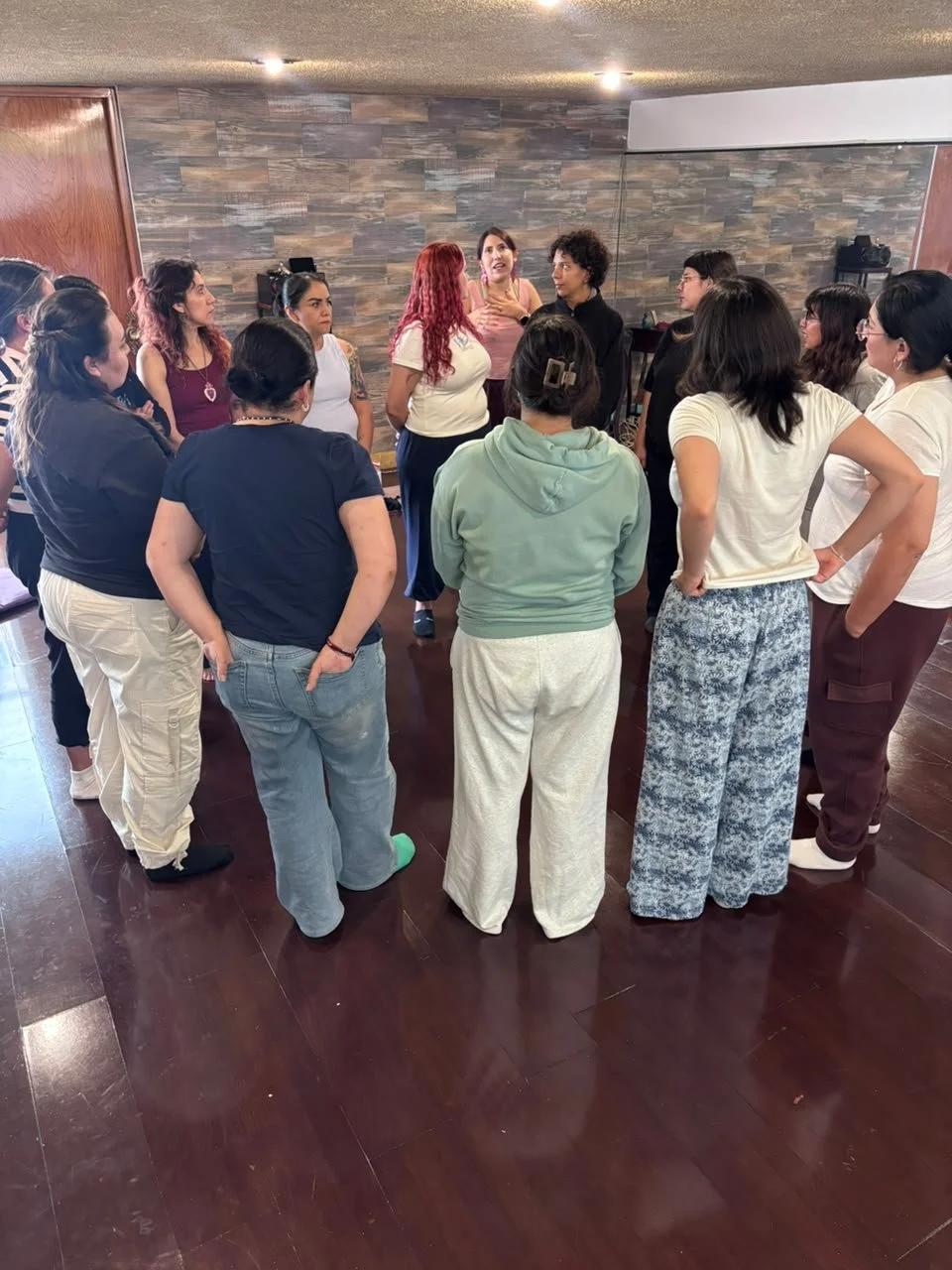 Grupo de personas en círculo en una sala de entrenamiento o reunión, conversando atentamente.