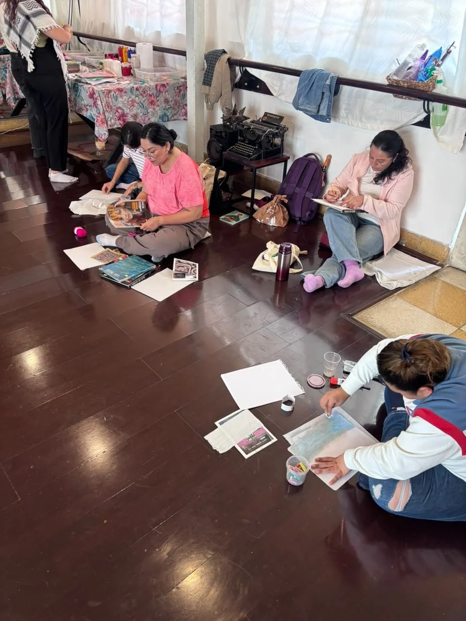 Varias personas sentadas en el suelo, leyendo y dibujando, en un ambiente interior.