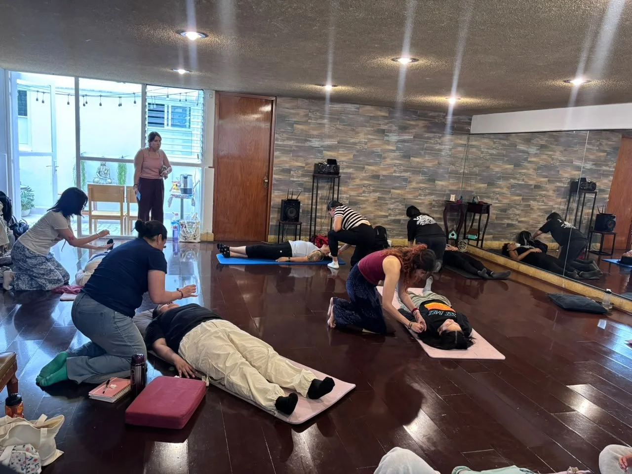 Grupo de personas participando en un curso de reanimación cardiopulmonar (RCP) en un salón con suelo de madera y paredes de piedra.