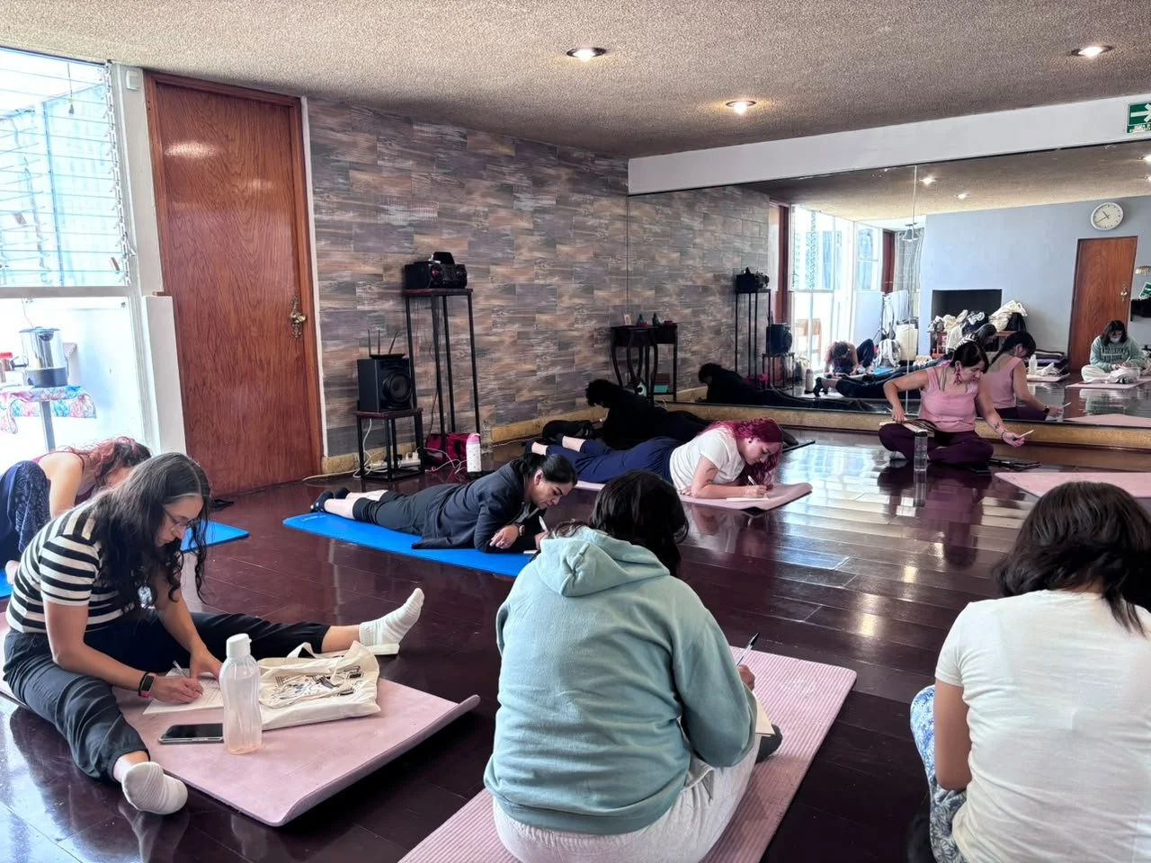 Grupo de personas participando en una clase de yoga en un estudio con paredes de piedra y ventanas grandes.
