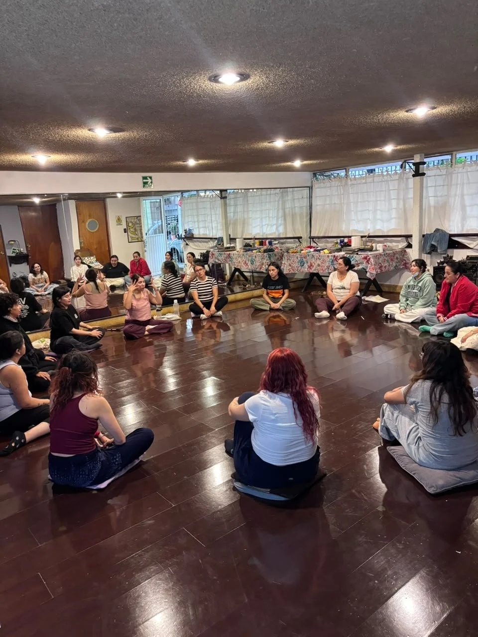 Grupo de personas sentadas en círculo en una sala, algunas con ropa casual y otras en pijamas, participando en una actividad grupal.