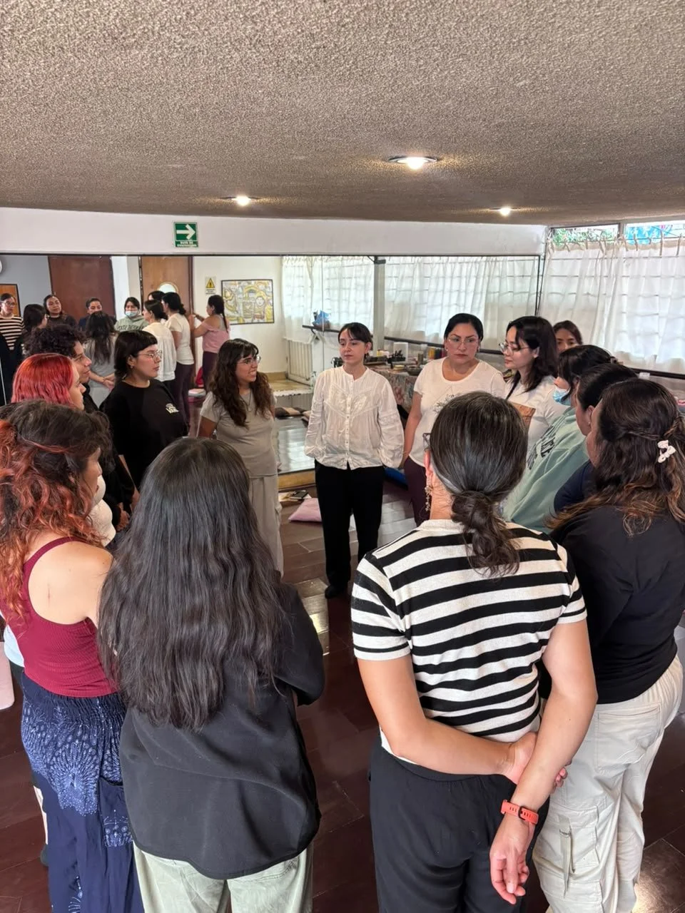 Grupo de mujeres en círculo en una reunión en interior, participando en una discusión o taller.