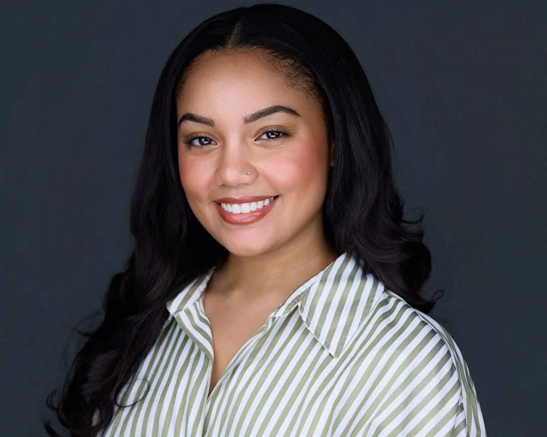 Portrait of a smiling woman with long black hair and a striped shirt against a dark background.