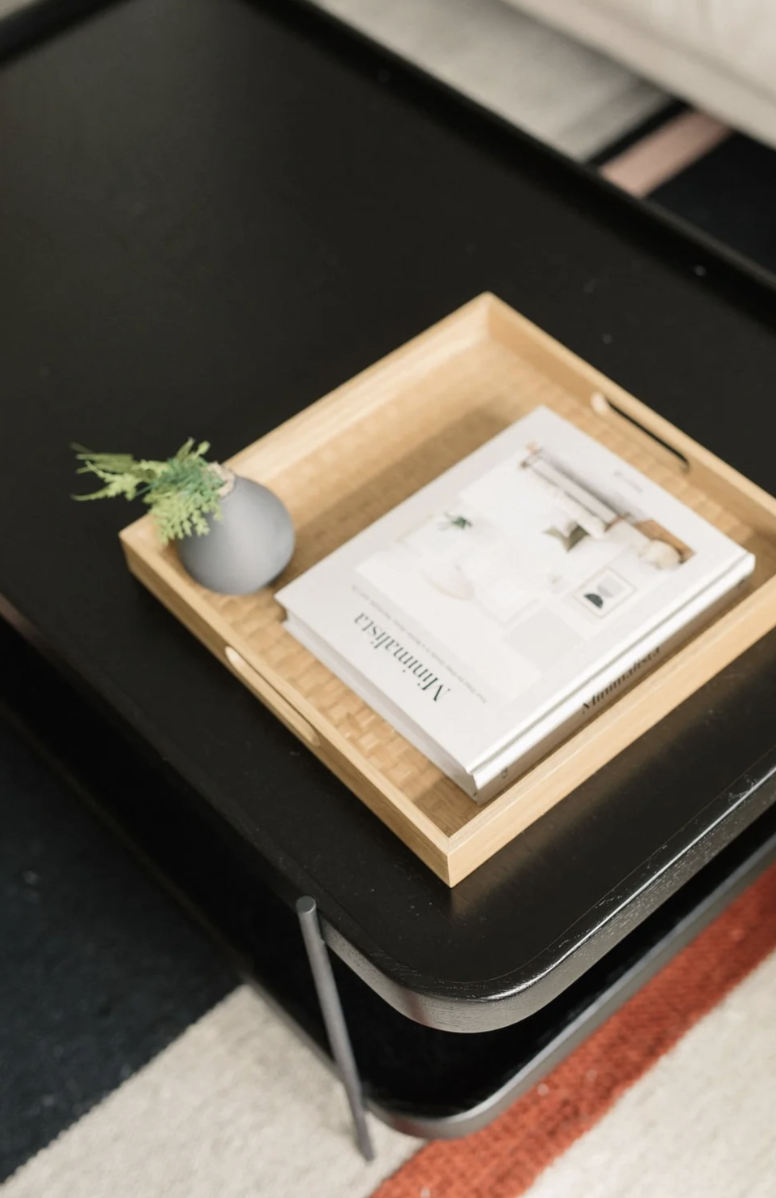 A wooden tray with a small gray vase containing green plants, and a stack of magazines or catalogs on a black table."Yaletown, Vancouver, BC interior designer and decorator North Vancouver, BC interior designer and decorator West Vancouver