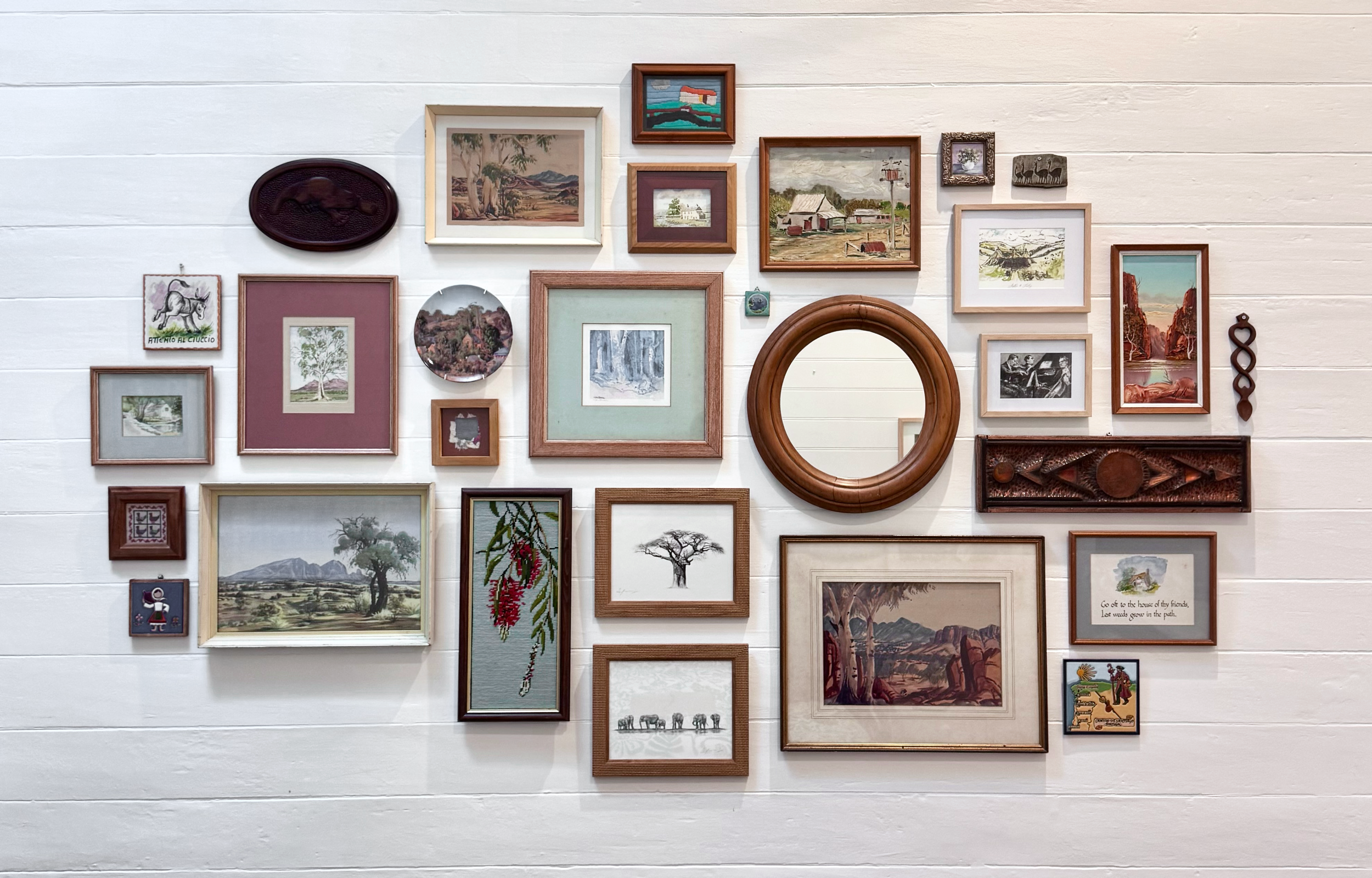 A white wall decorated with a variety of framed pictures and artwork, including landscapes, trees, animals, and abstract designs.