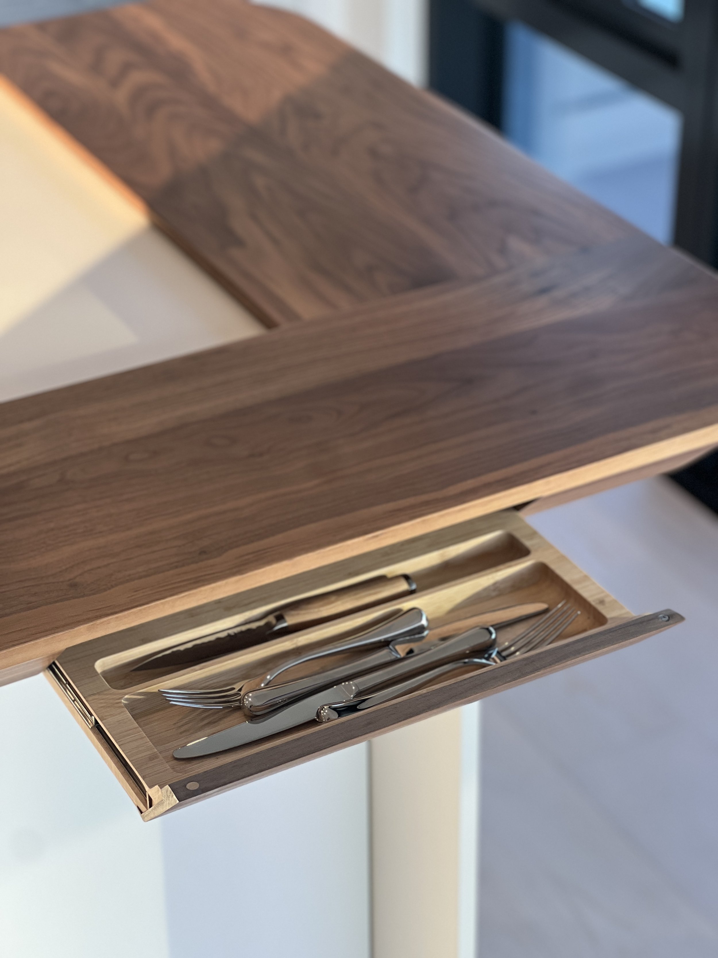 Two nested drawers with hand-carved cutlery organizers provide hidden storage, maintaining the island's clean lines while adding practical functionality for daily use.