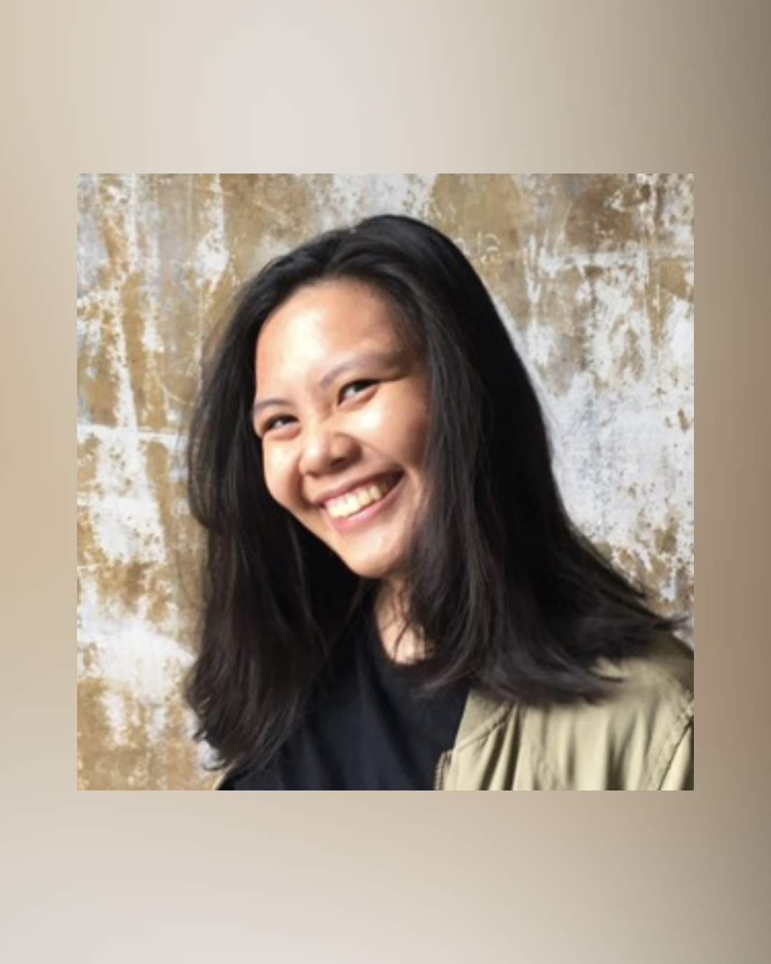 A young woman with long black hair smiling and looking at the camera, standing in front of a textured beige and white wall.