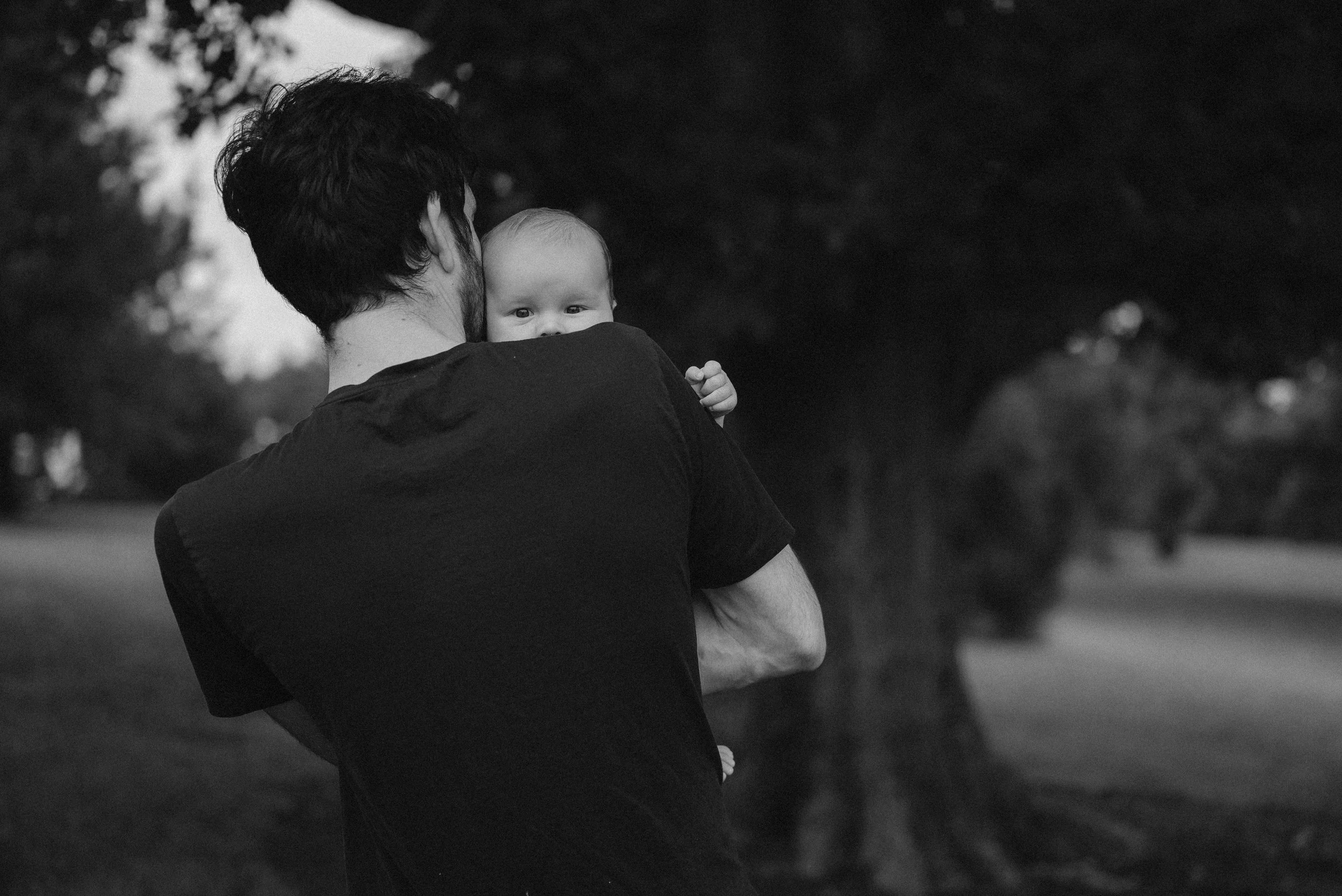 A dad holding a baby on his shoulder during an outdoor lifestyle family photoshoot.