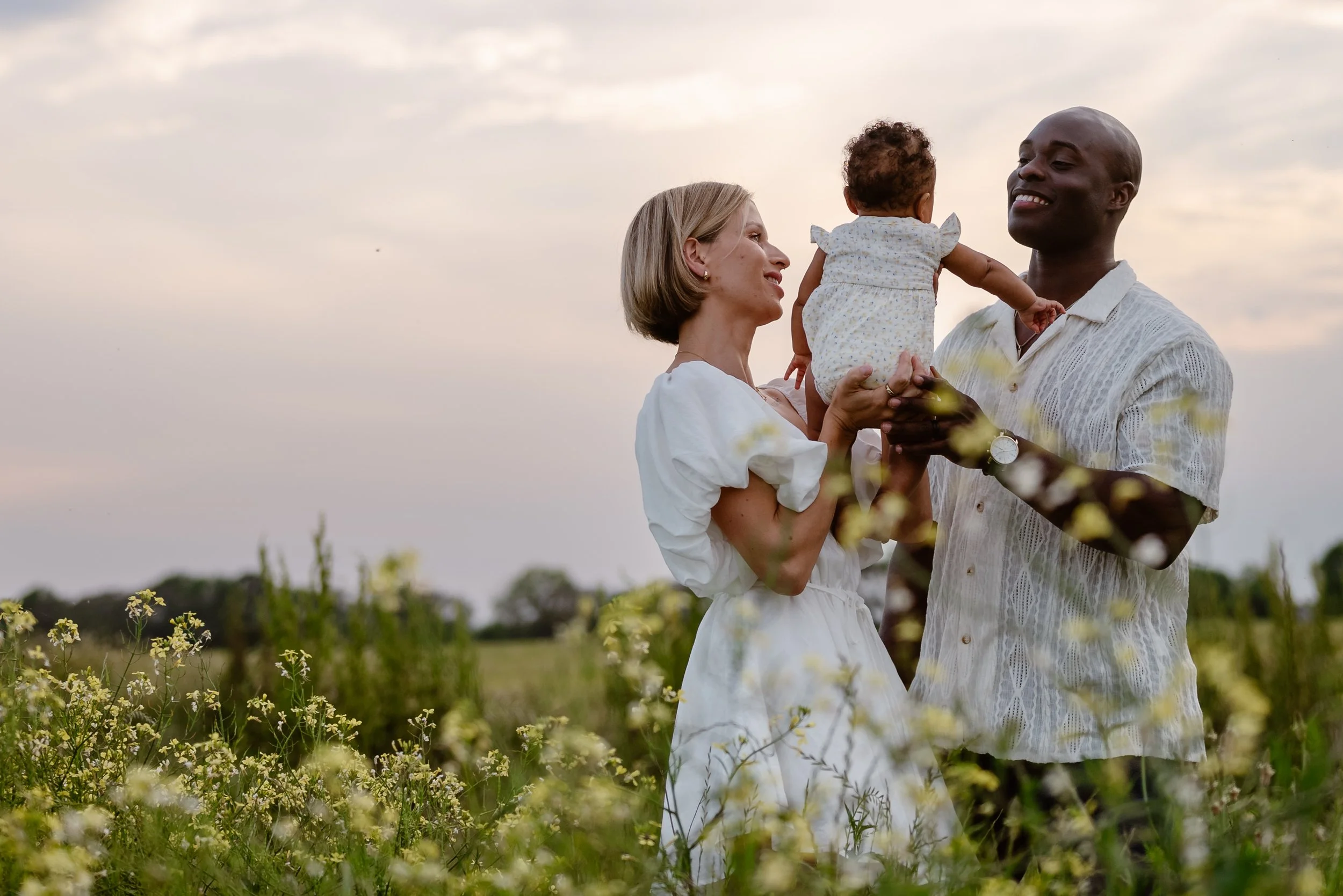 A rustic boho couple holds their new baby in a field of flowers