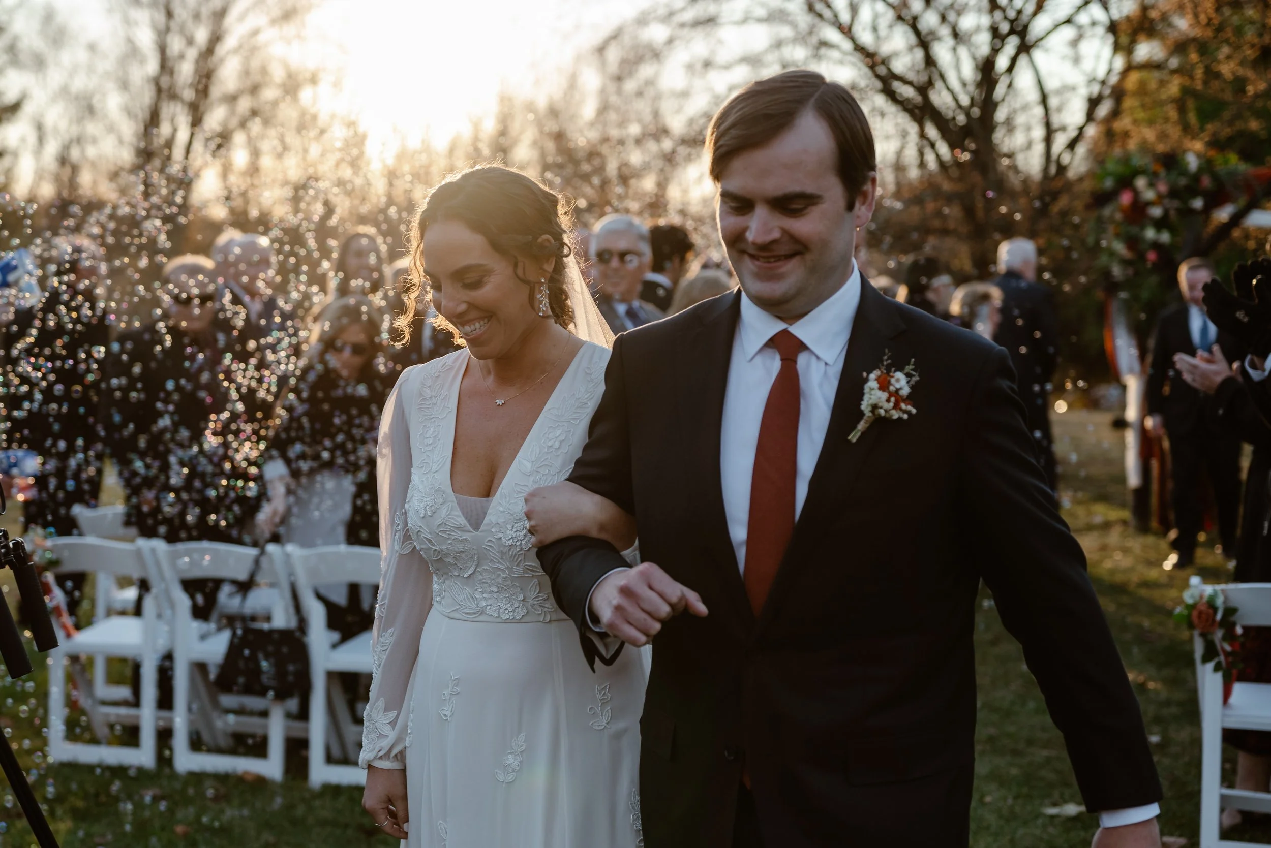 A husband a wife walk down the aisle at sunset during their fall small outdoor wedding ceremony