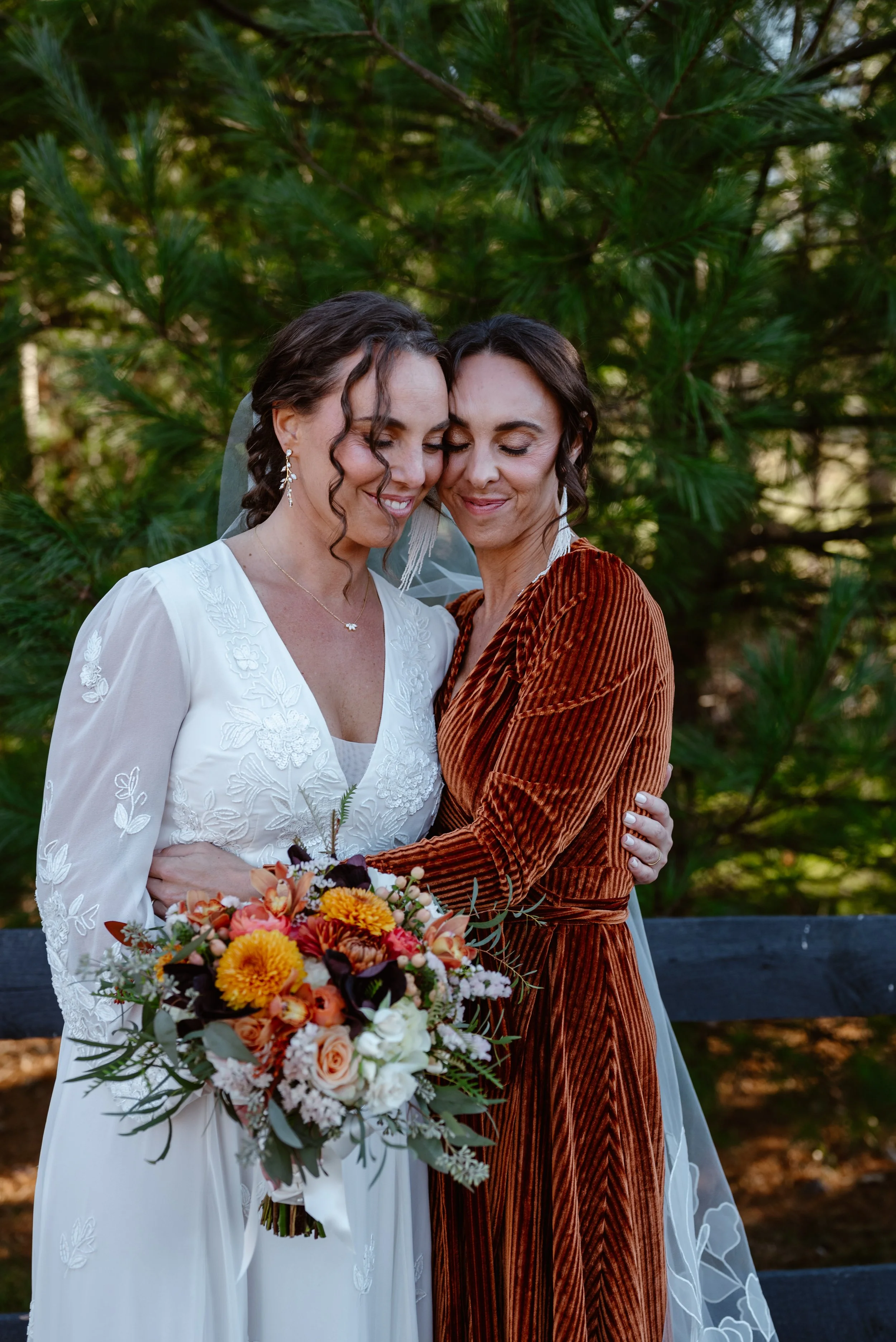 Two sisters embrace during a fall wedding photoshoot wearing western boho velvet bridesmaid dresses