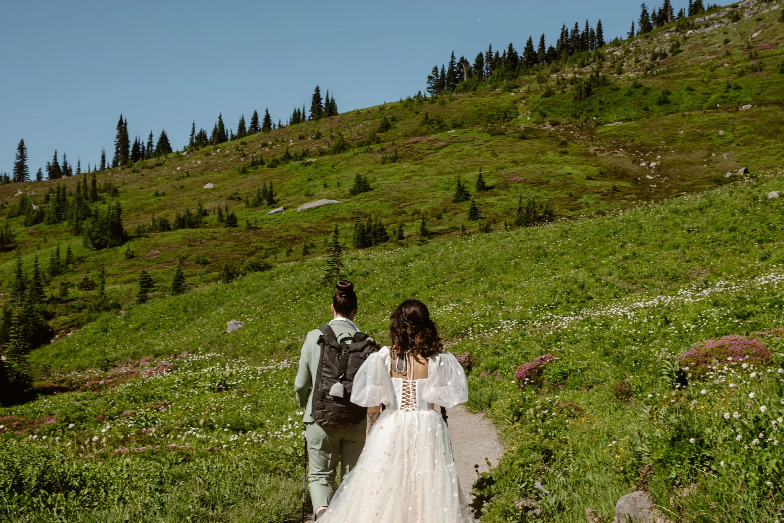 A LGBTQ+ couple hiking in wedding attire during a summer adventure elopement at Mt. Rainier National Park