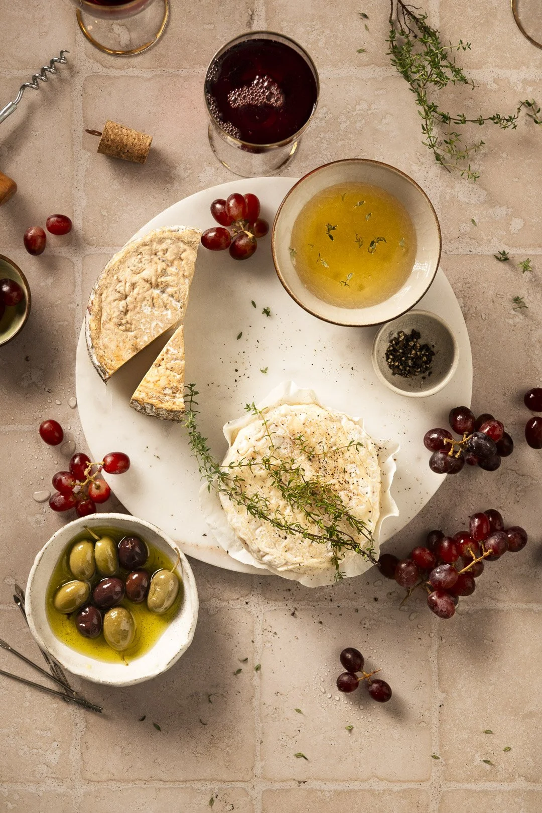 cheese board on wooden table and cut board, with fresh grapes, honey and olives, ready for sharing as appetizer with red wine