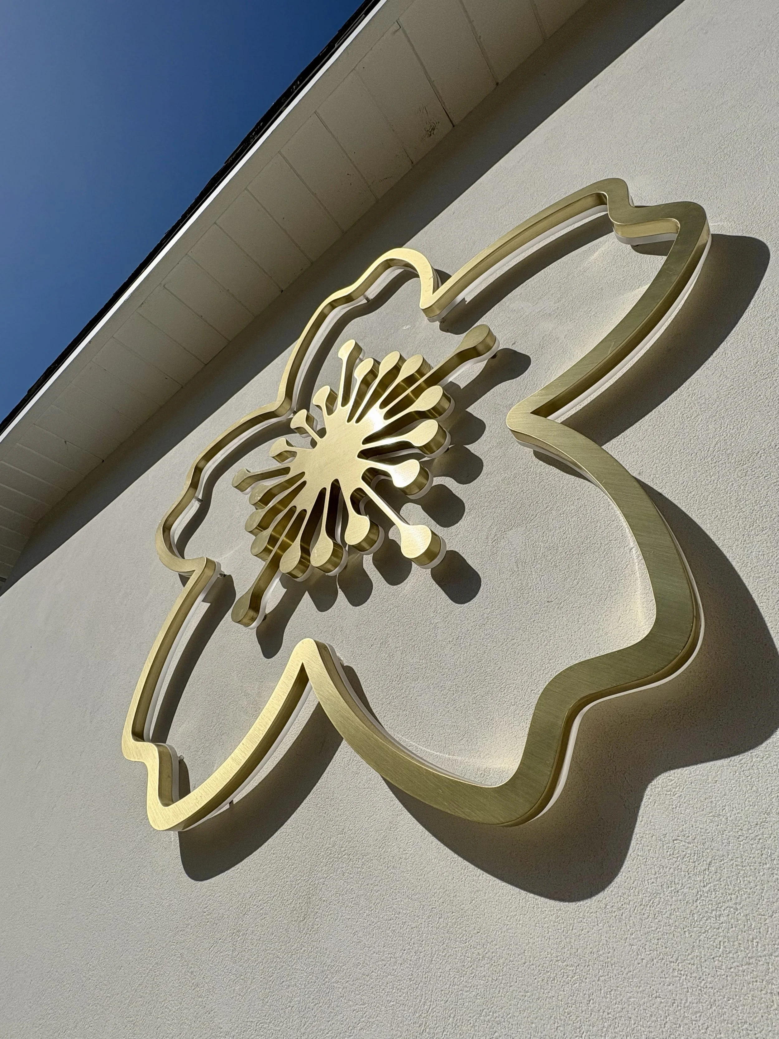 Gold metallic decorative sign of a flower and butterfly mounted on a beige wall outside building.
