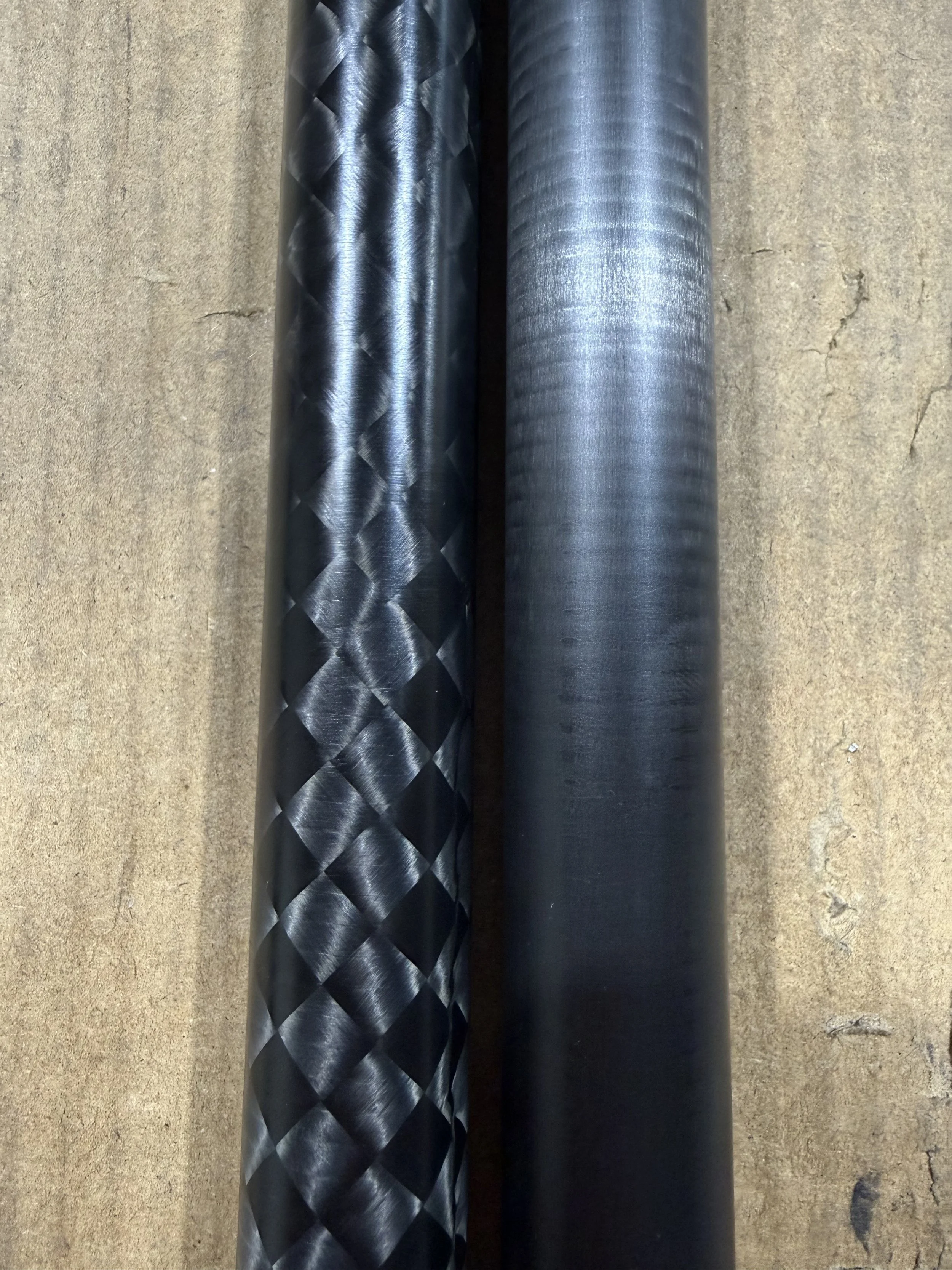 Close-up of two cylindrical metal tubes lying parallel on a concrete surface, one with a diamond-patterned texture and the other smooth and shiny.