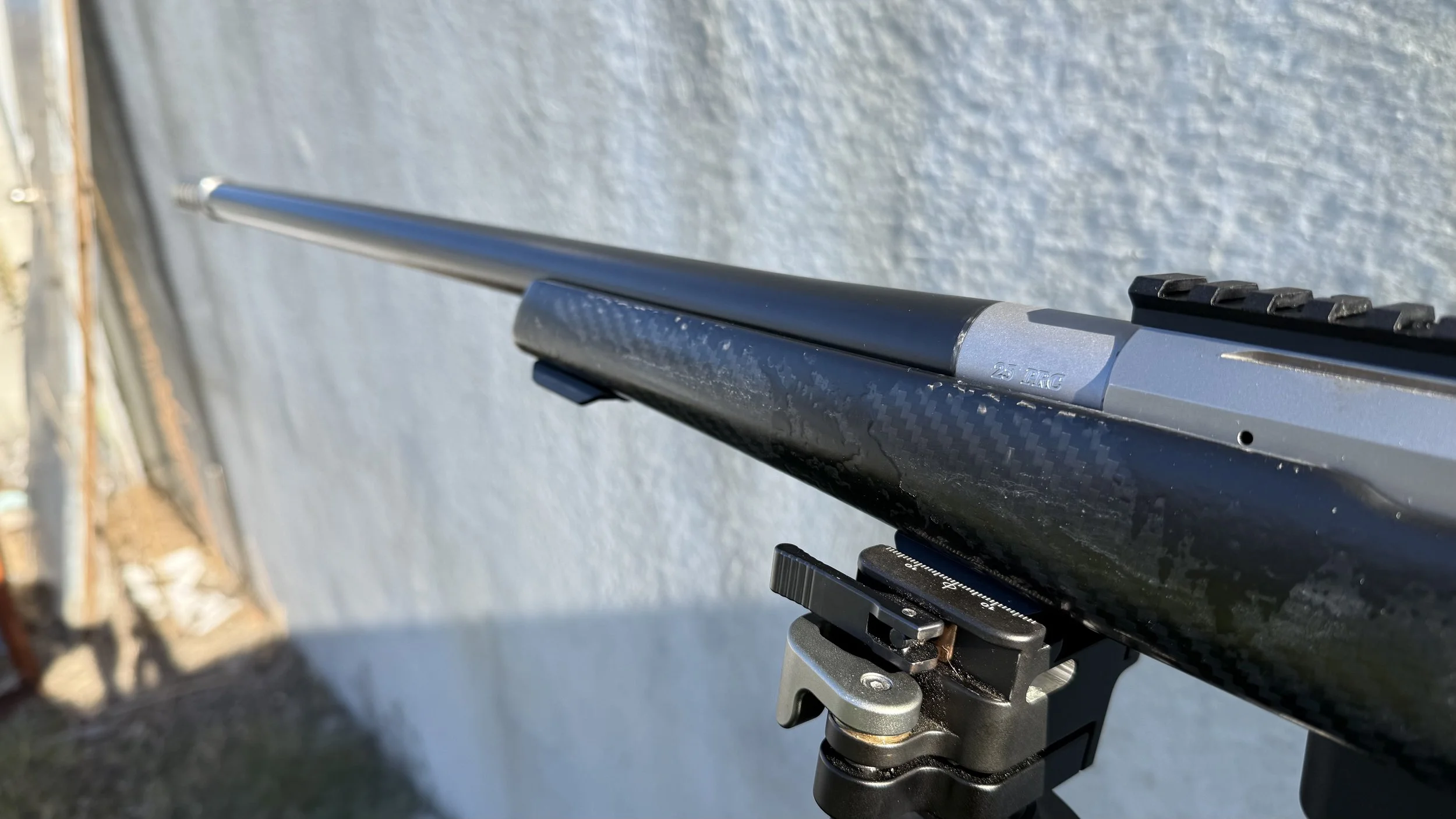 Close-up of a rifle scope mounted on a firearm, with a clear sky and outdoor setting in the background.