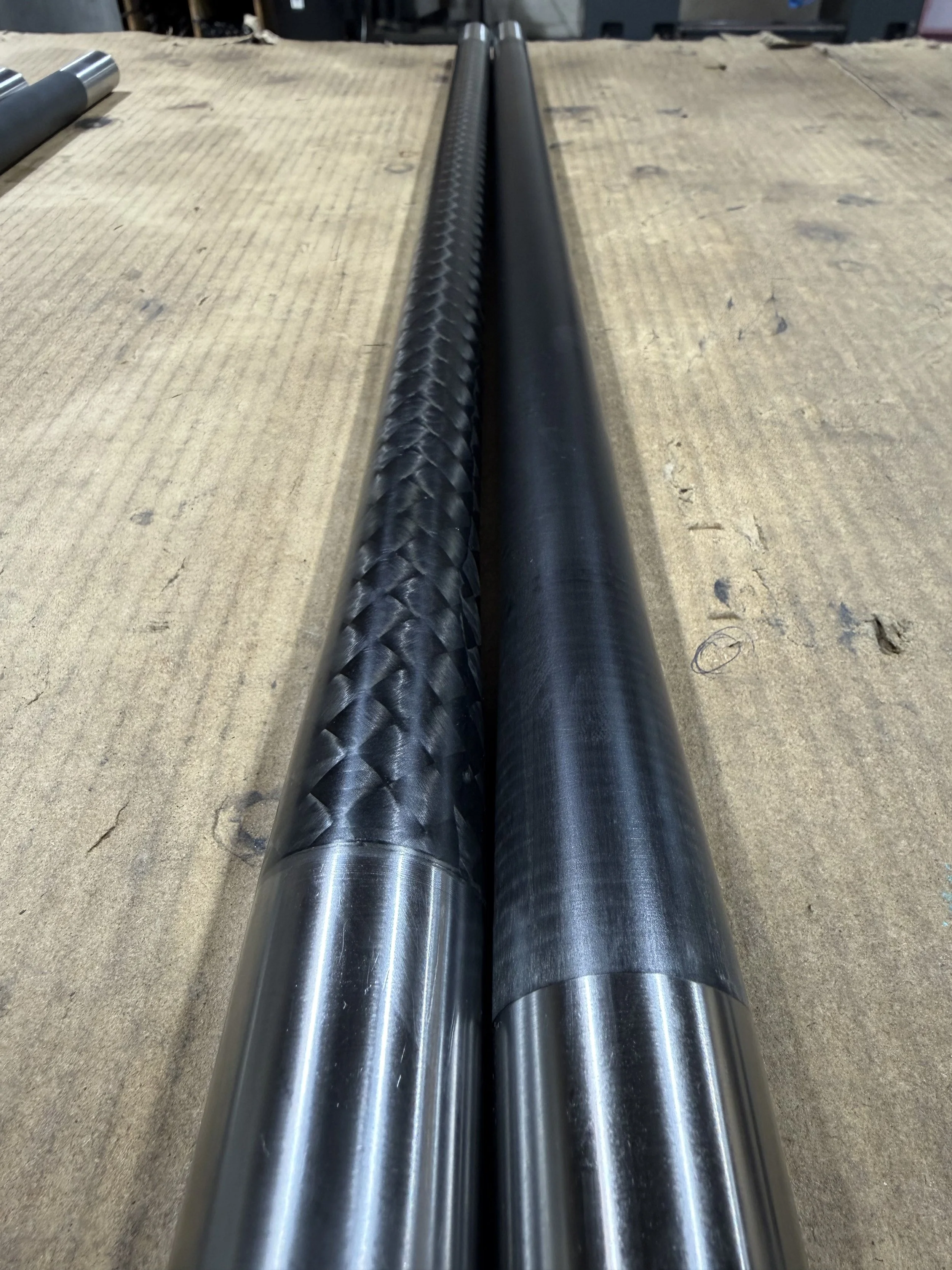 Two black metal pipes placed on a wooden workbench in a workshop.