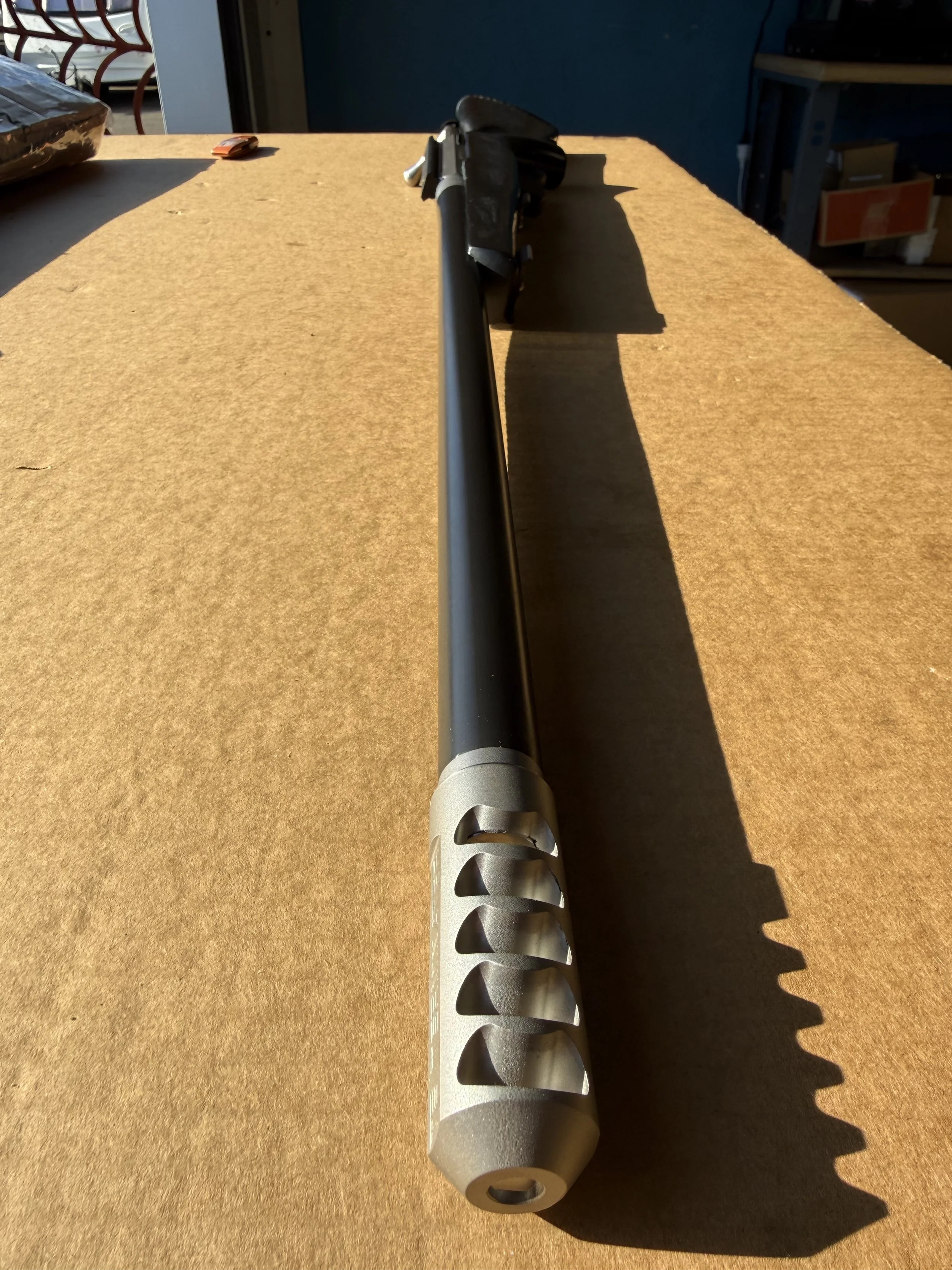A long metal flute with a series of curved holes in the side, resting on a wooden table in sunlight.
