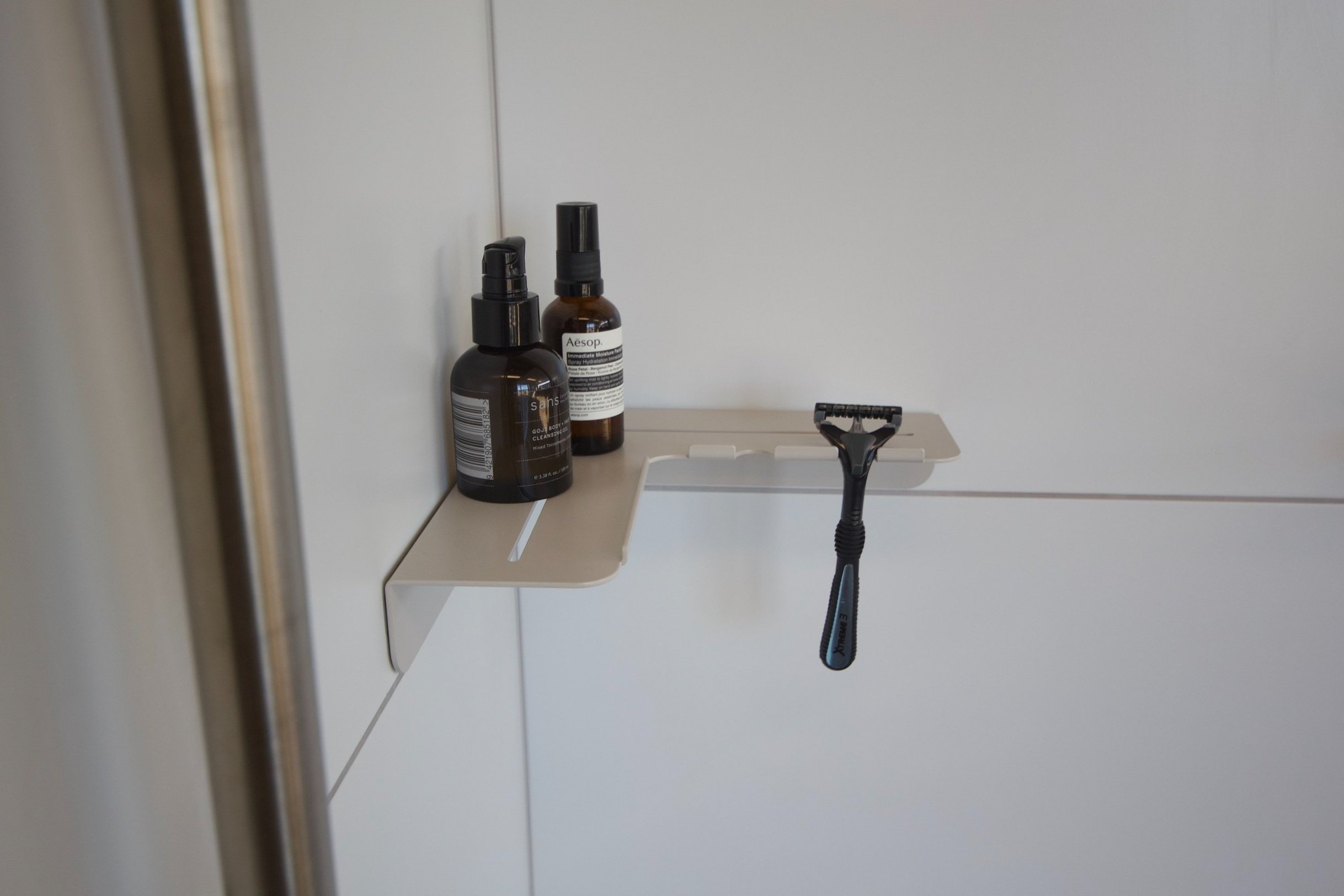 A razor hanging on a wall-mounted shelf with two bottles of skincare products next to it.