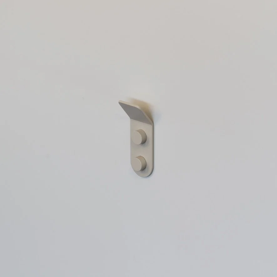 Minimalist beige aluminum wall hook photographed in a studio for a product shot.