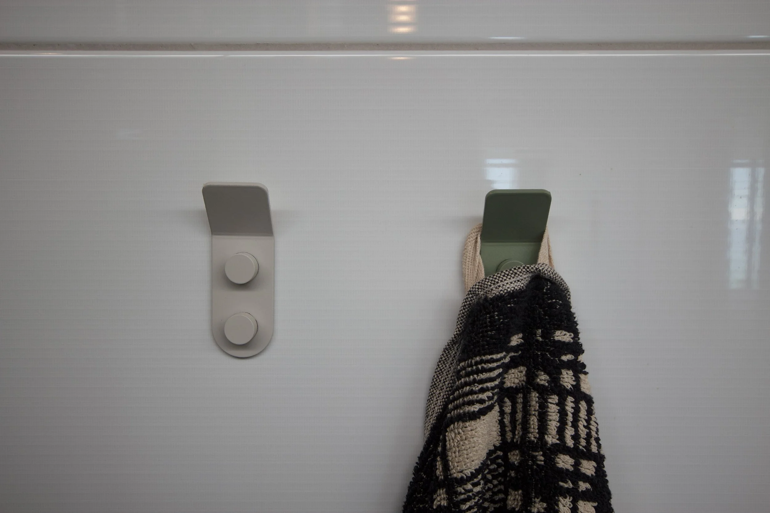 A white wall with two hooks: one empty and one holding a scarf and a black-and-white patterned item.