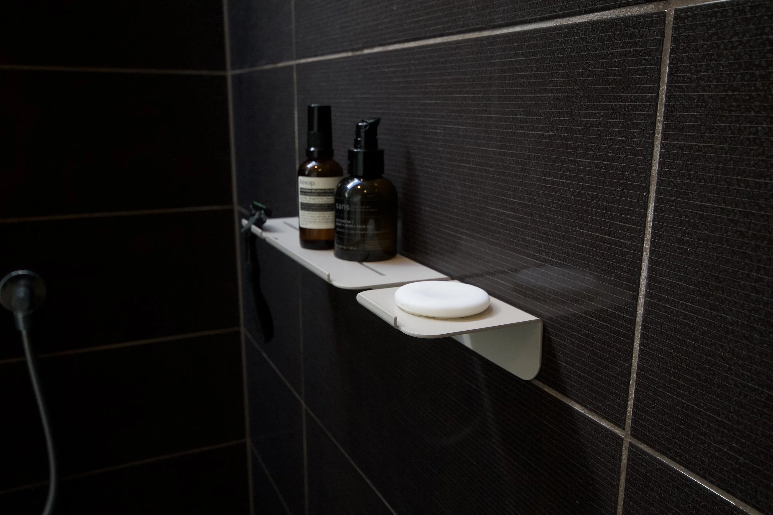 Shelves with personal care products and a soap in a bathroom with black tiled walls.