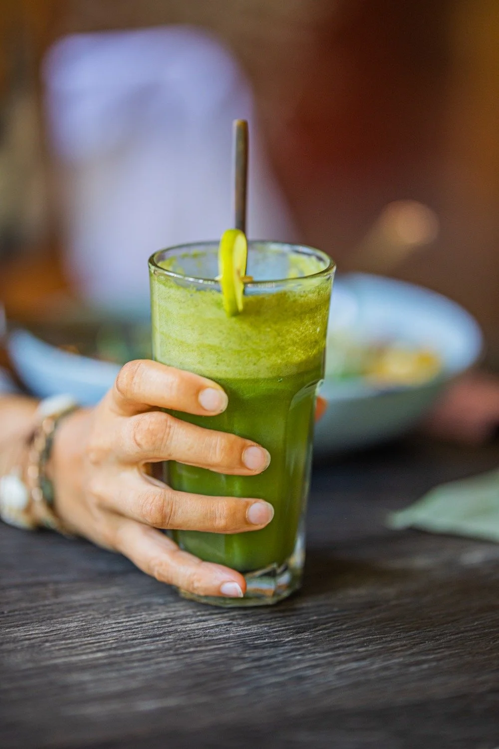 Hand holding a green smoothie in a glass with a lemon slice on the rim