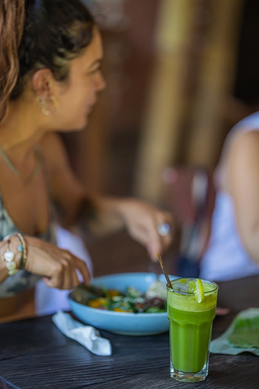 Close-up of a Charlotte eating a salad with a glass of green juice and a lime wedge on the table.