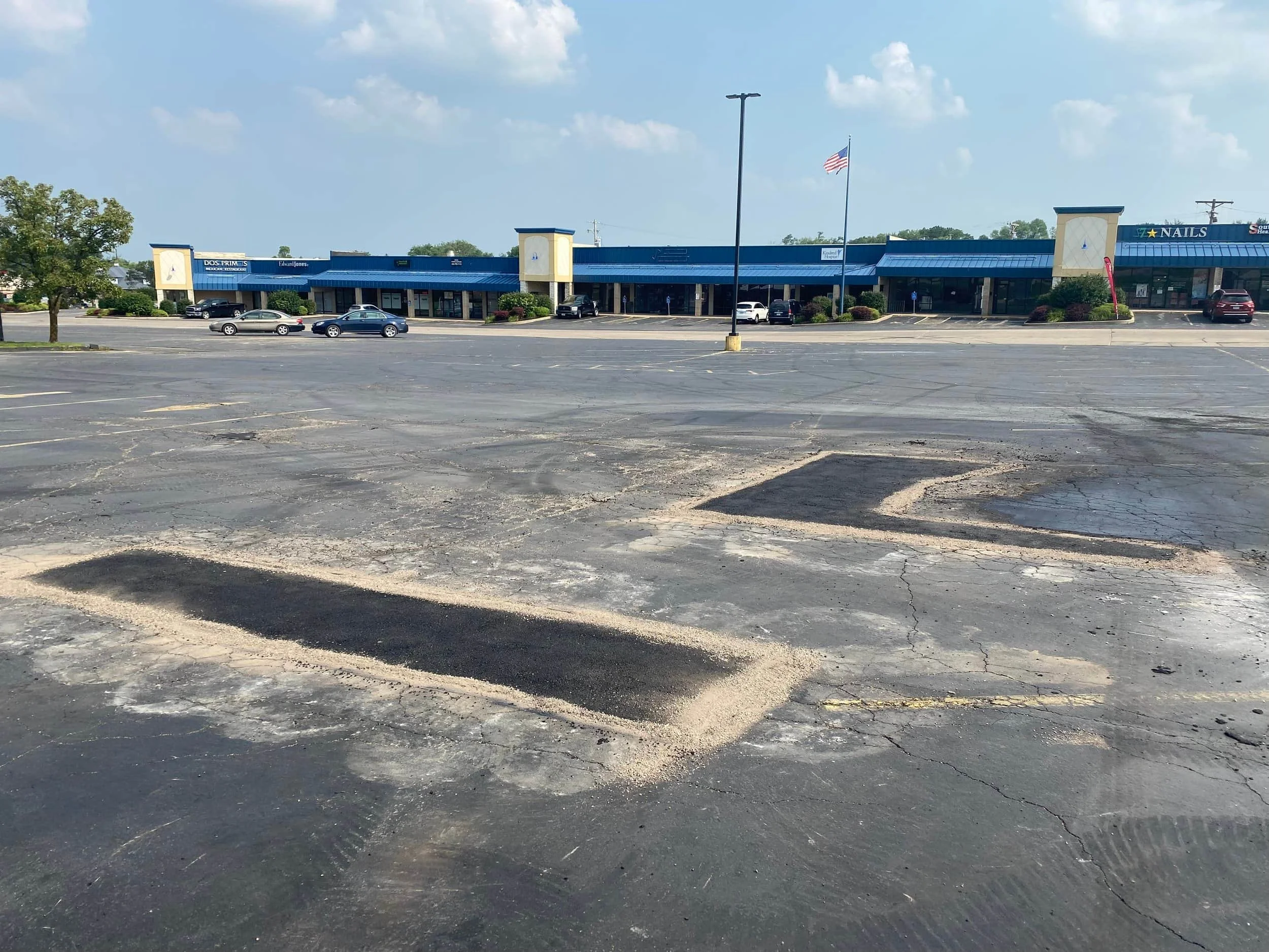 Broken and old parking lot has a new fresh asphalt patch. The patched areas are a bit darker than the rest of the asphalt around it.