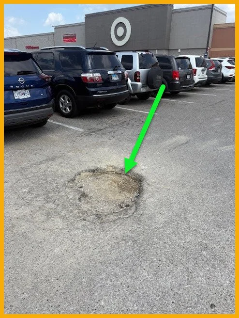 Large pothole in a parking lot, highlighted by a green arrow, with cars and a Target store in the background.