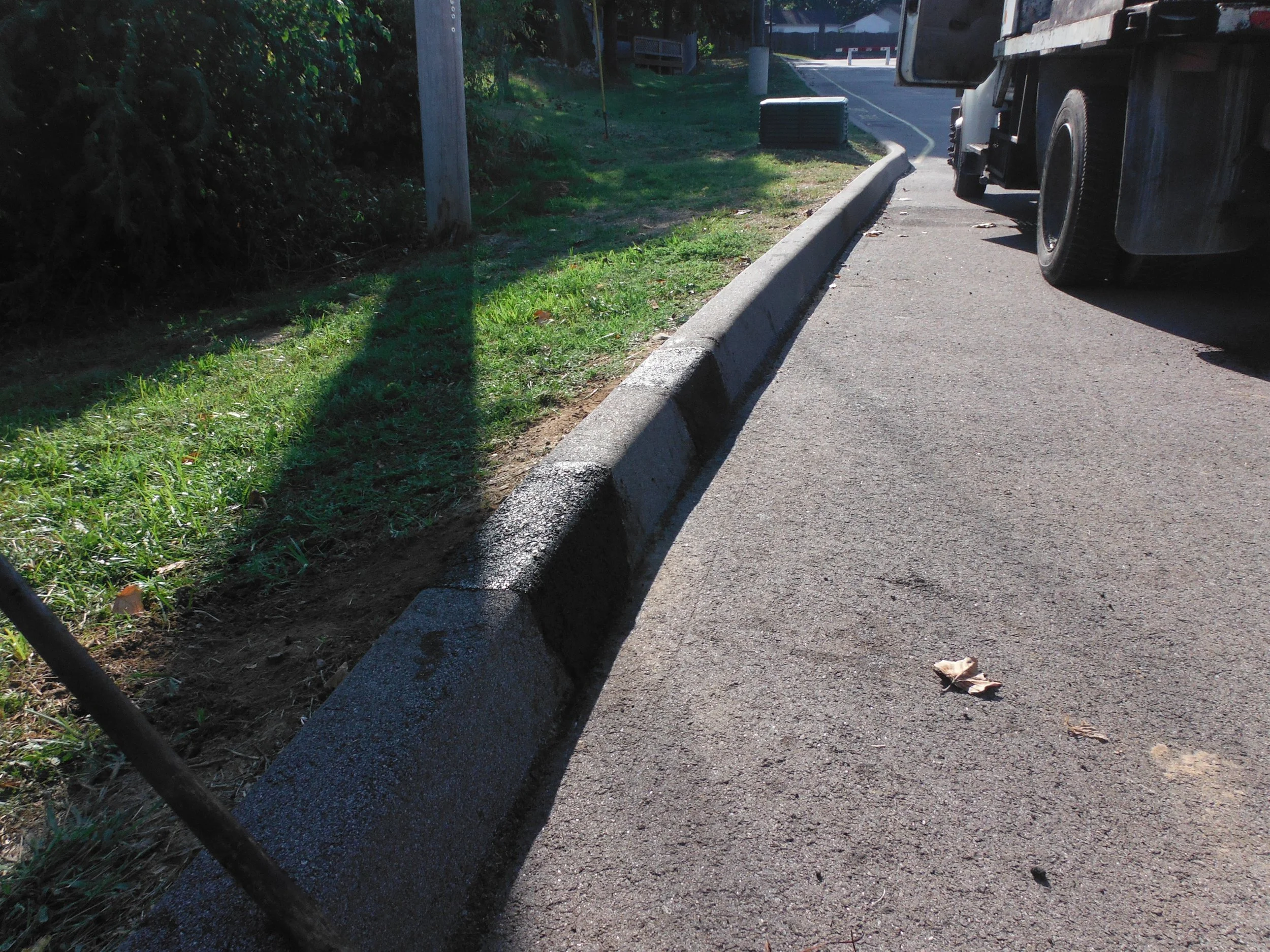 A street curb with a grassy area beside it, a utility box, and part of a large truck parked on the street.