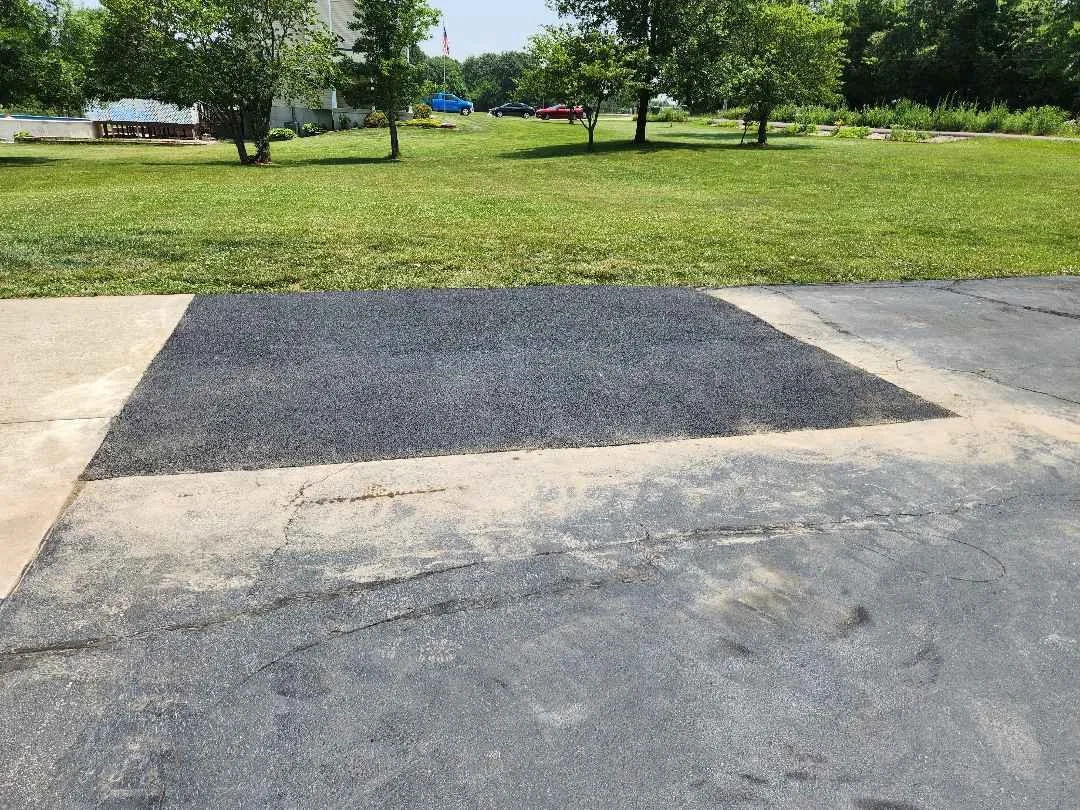 Broken asphalt on a drive that is repaired to one solid piece and the seams no longer show cracks. green grass in the background on a sunny day