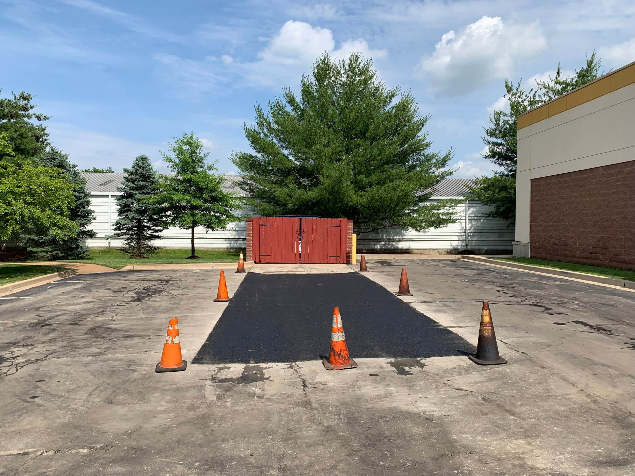 fresh parking lot patched in ballwin mo. cones mark off the finished work zone. Very bright blue skys and very dark new blacktop. Ballwin Mo