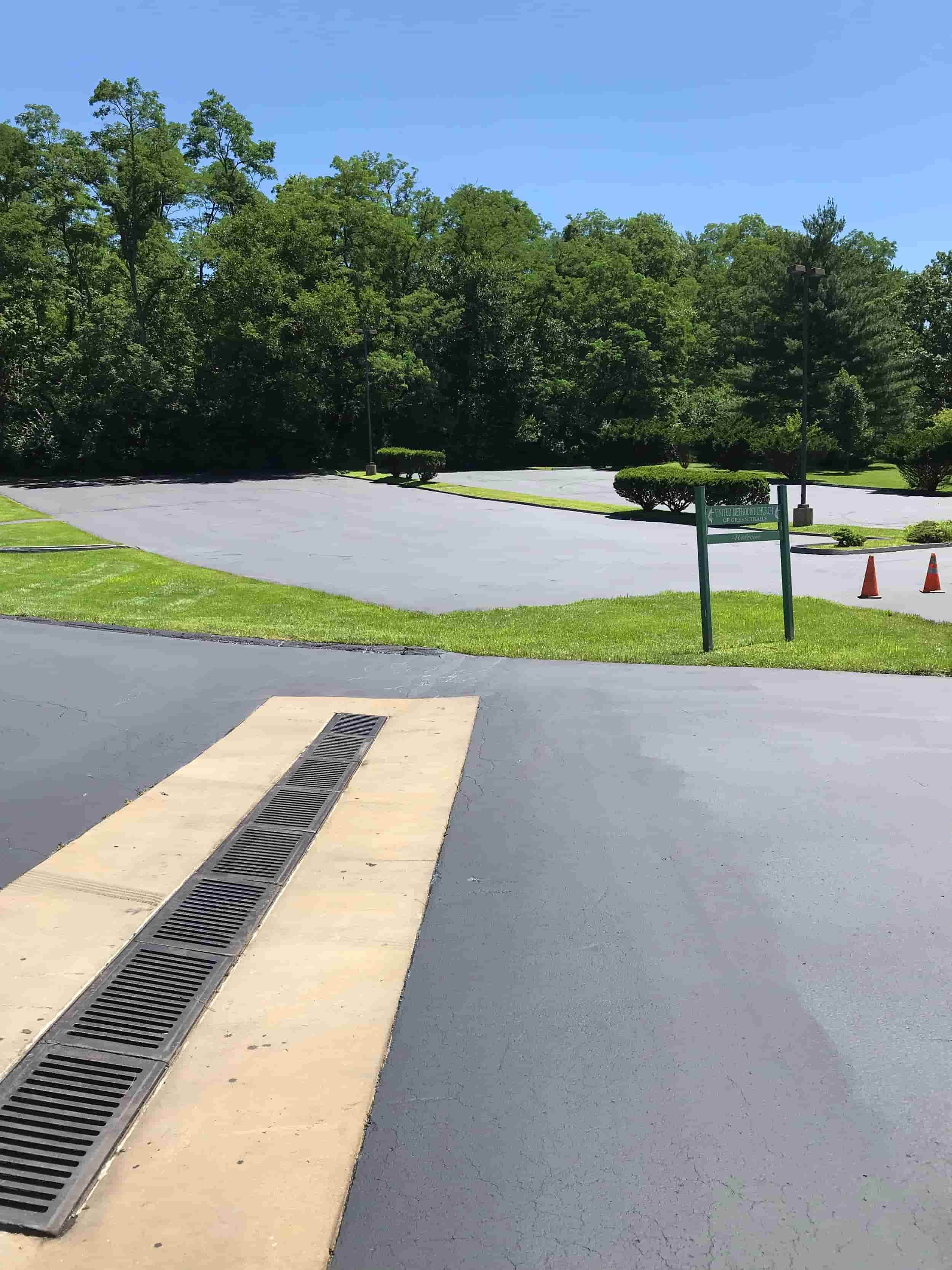 Empty parking lot surrounded by greenery and trees with a sign and two orange traffic cones.